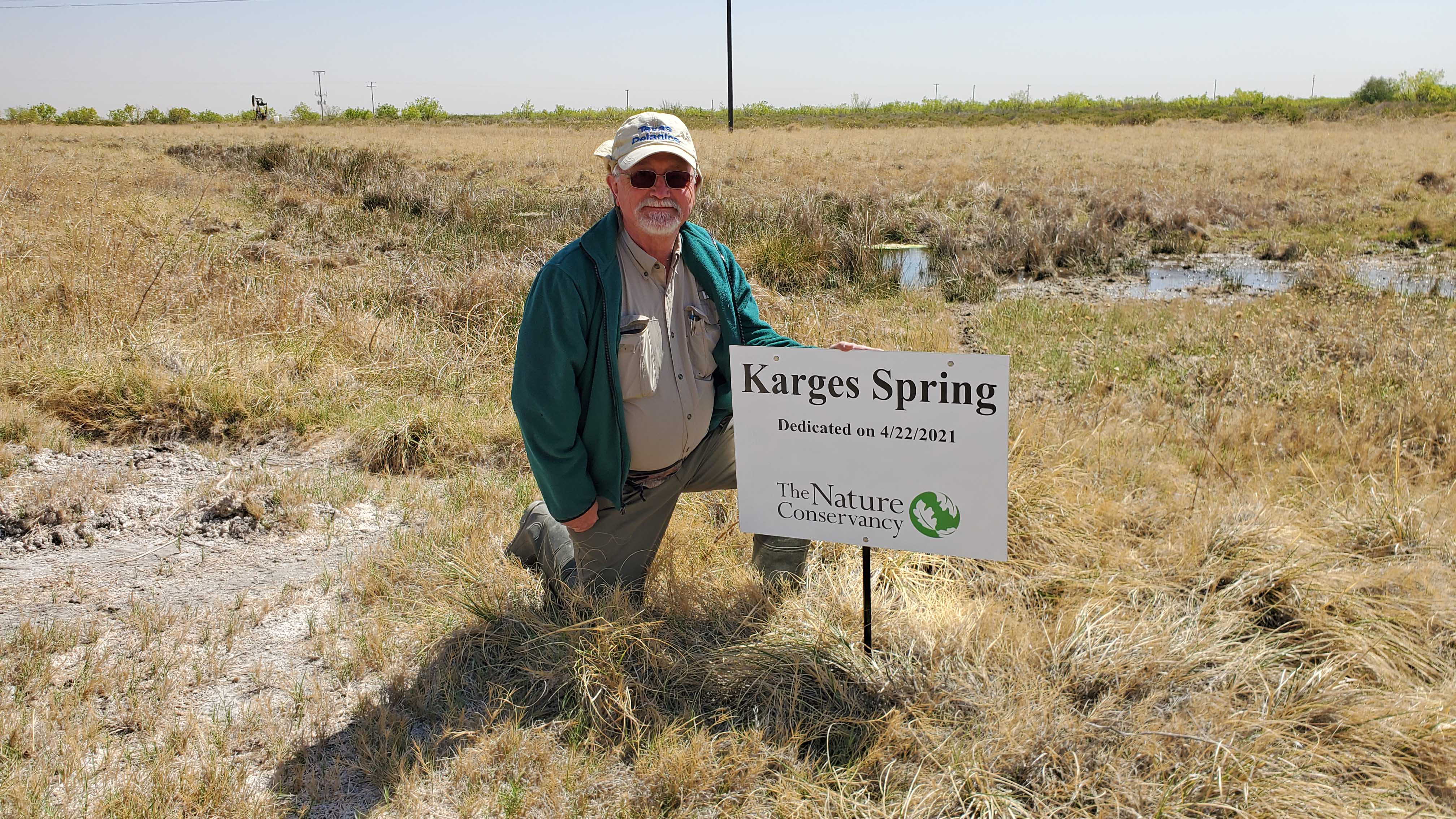 A man kneels beside a sign reading Karges Spring.
