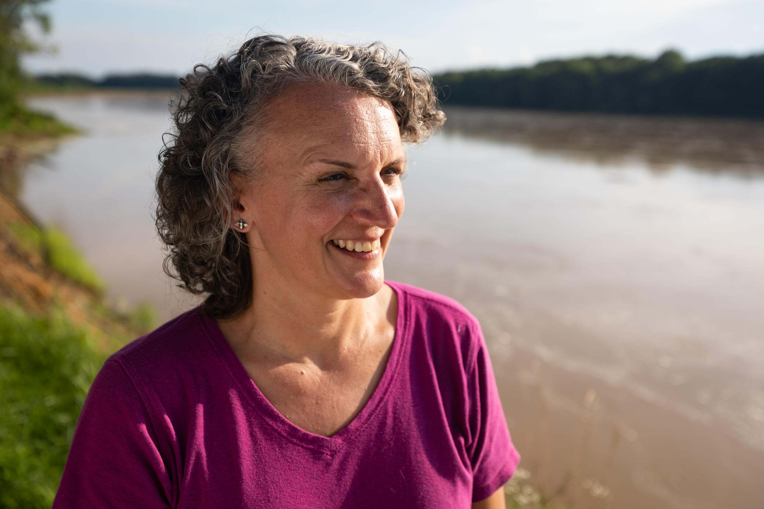 A woman in a maroon shirt standing by a river. 