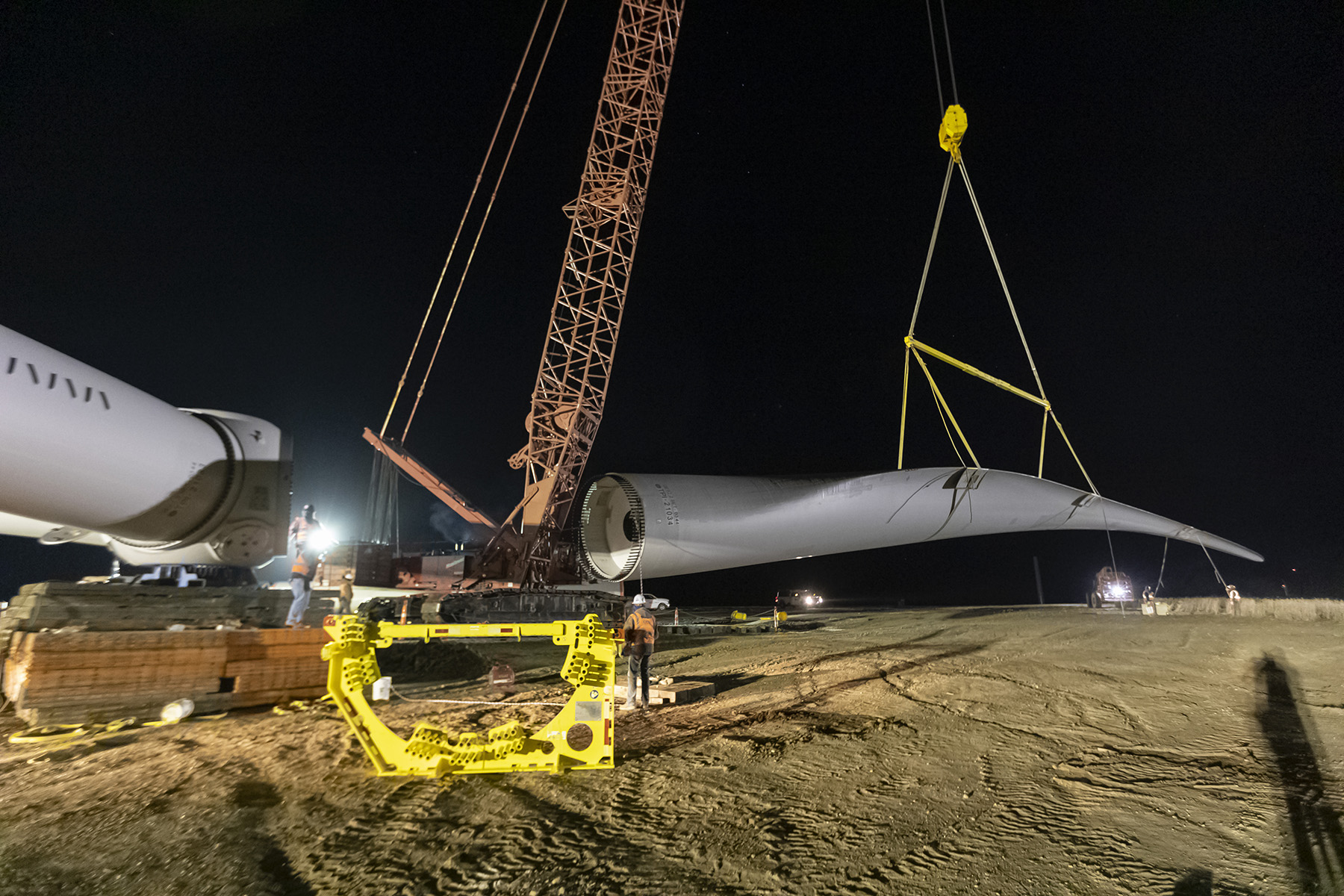 Men installing wind turbine blade at night.