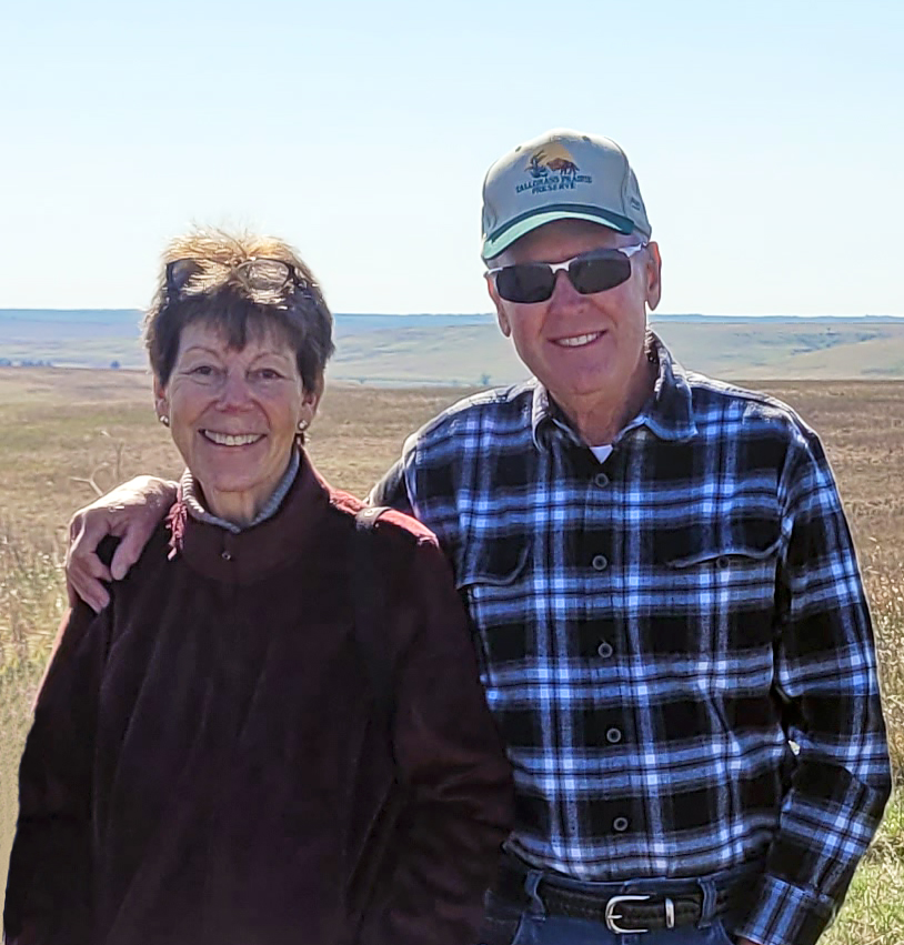 A couple smiles in front of a prairie landscape.