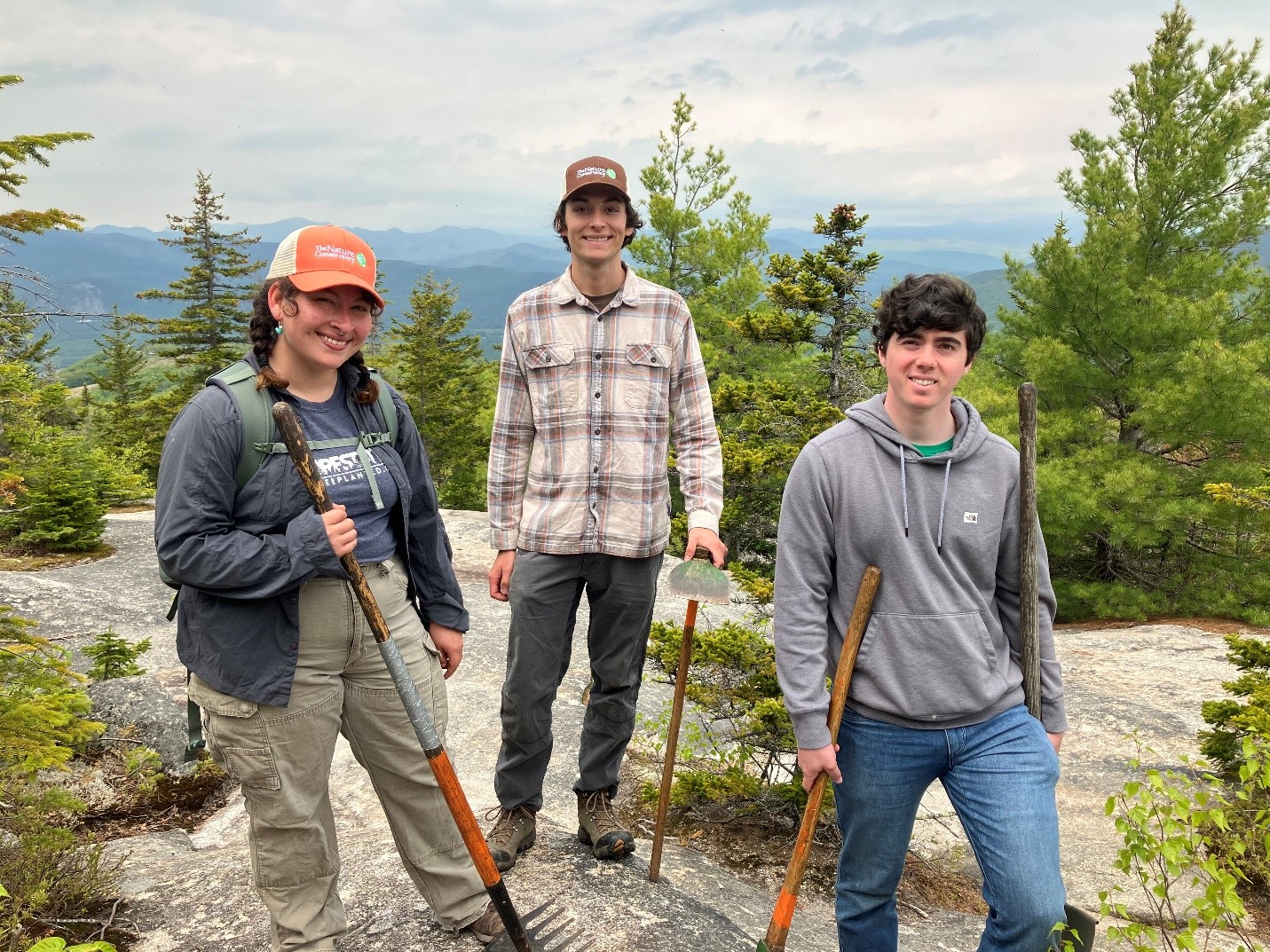A young woman and two young men in field clothes standing at the top of a mountain.