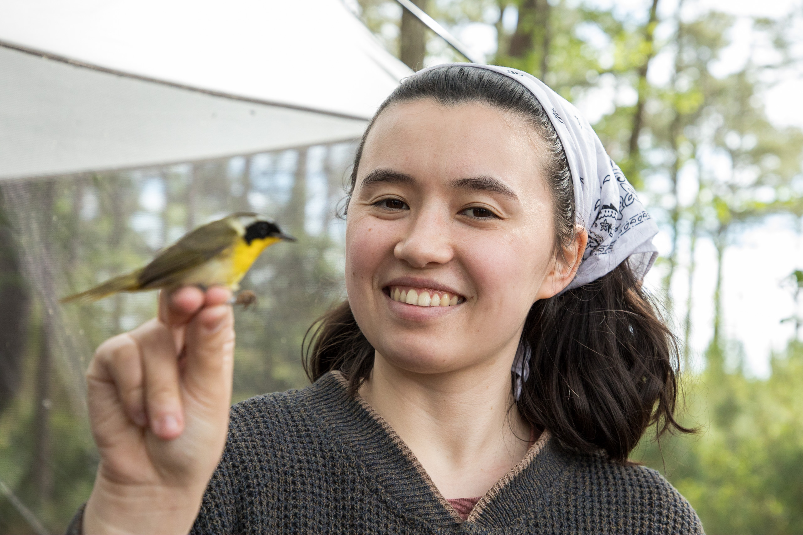 A smiling woman holds a small bird by its feet. 