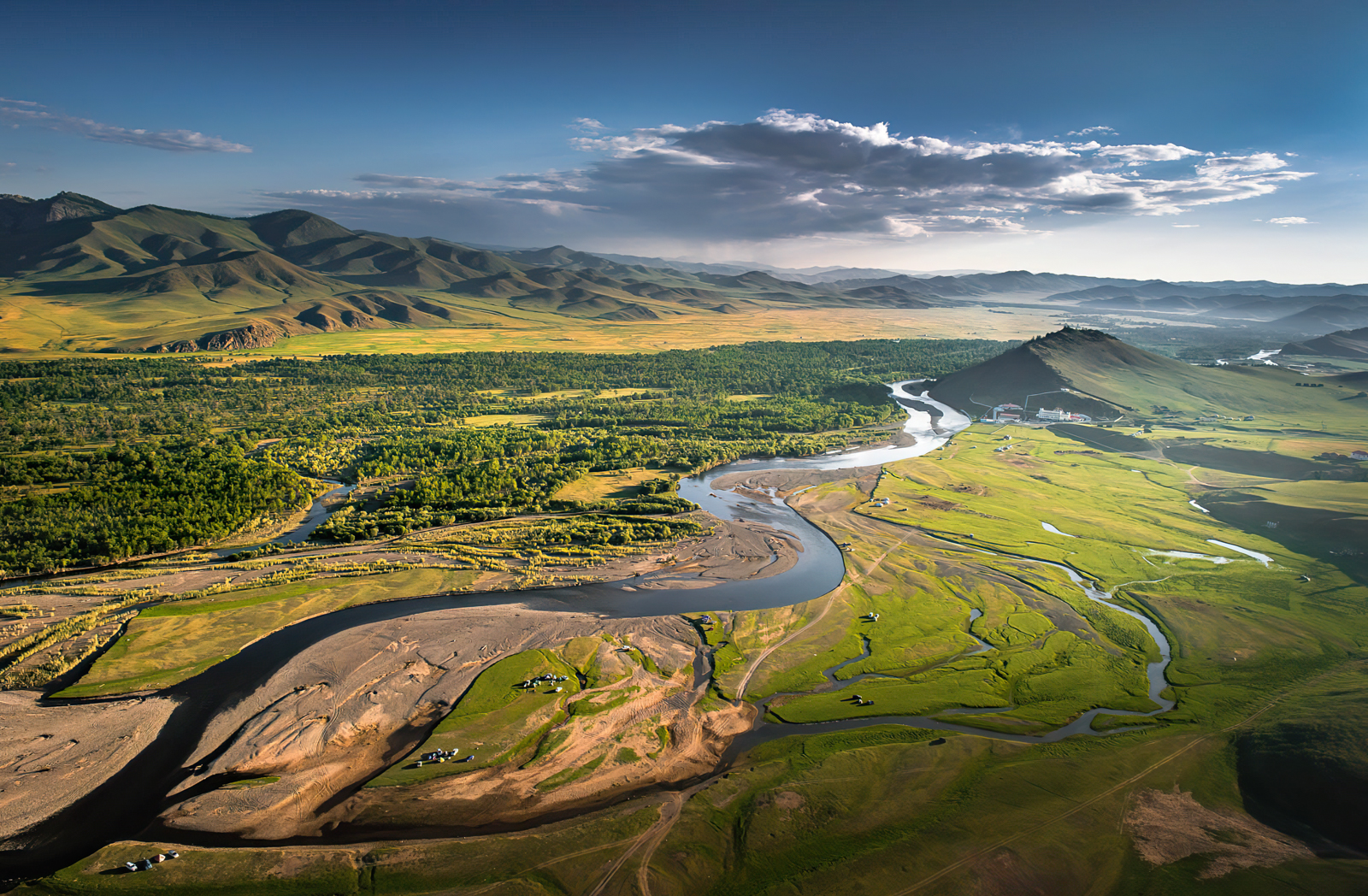 A river meanders through a forested valley with mountains in the background