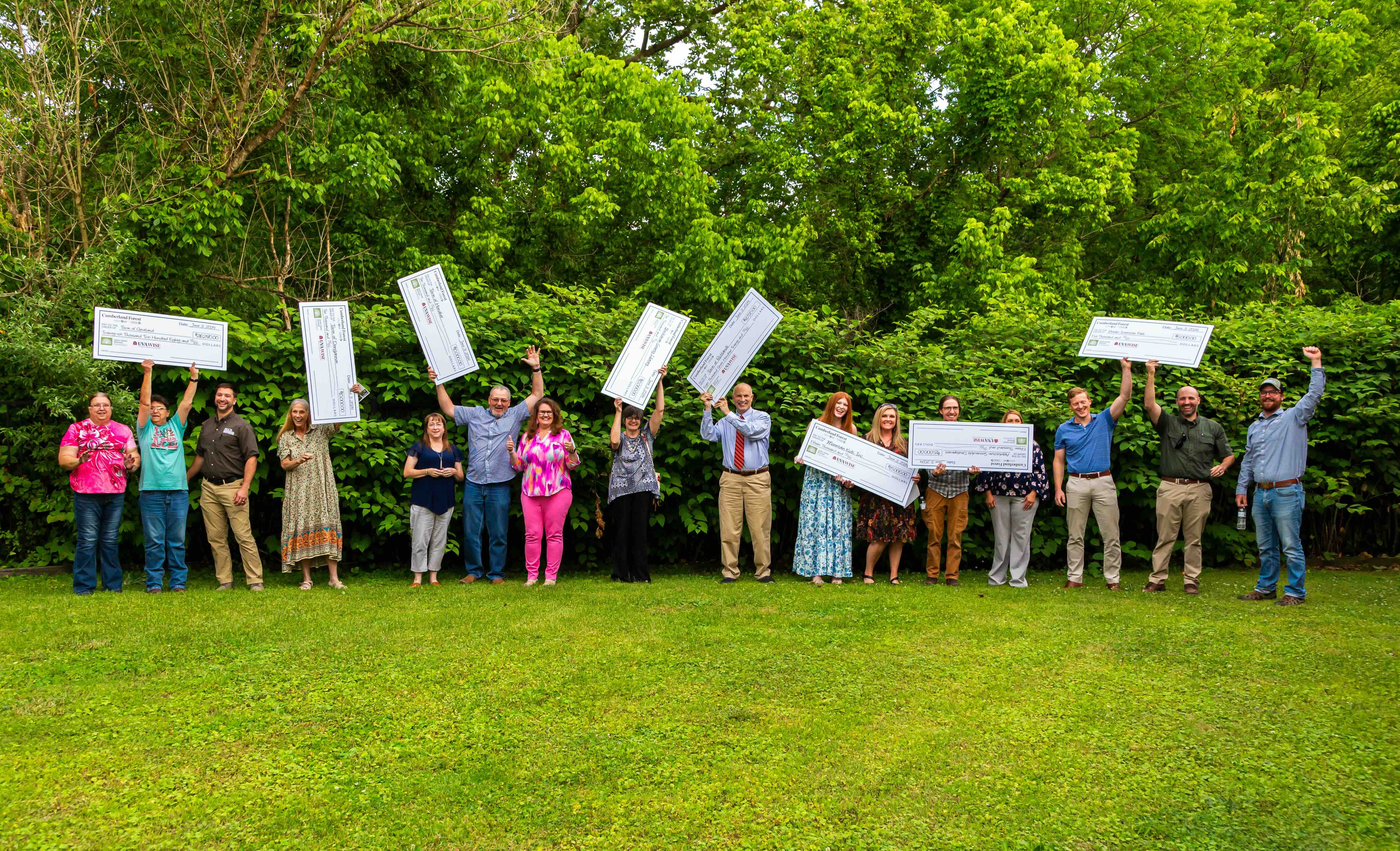 A group of people holding giant checks stand in a line outdoors.
