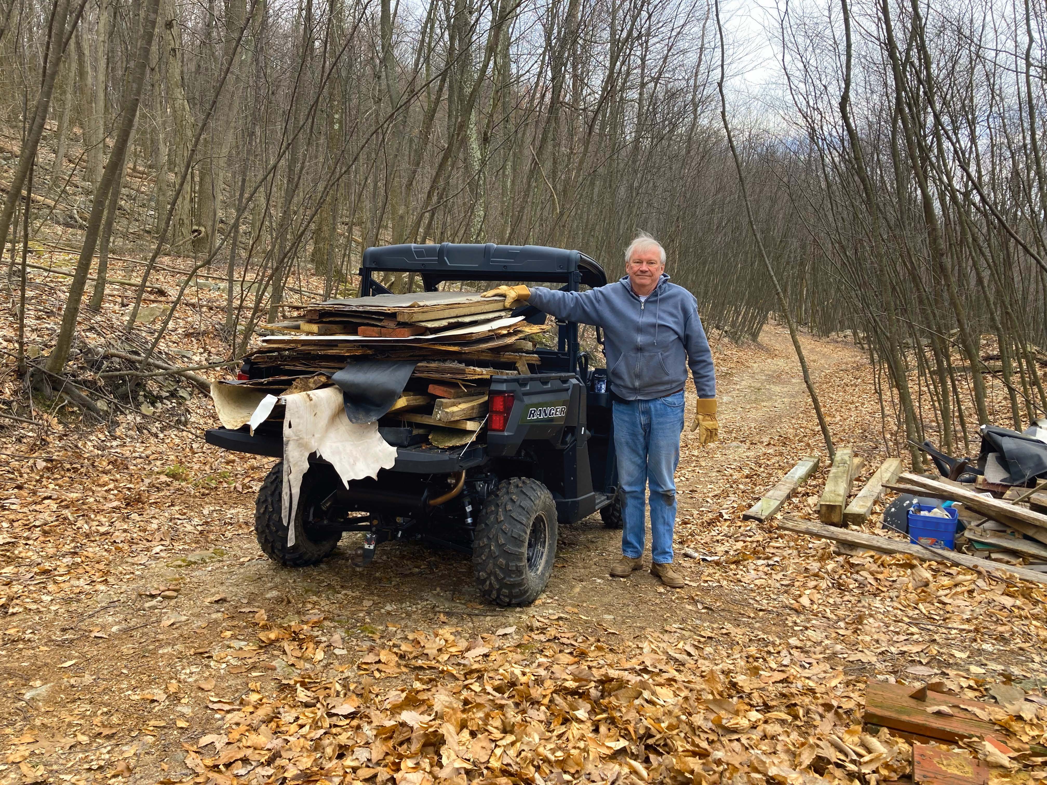 A person stands next to a vehicle with large piles of wood in the trunk in the forest.