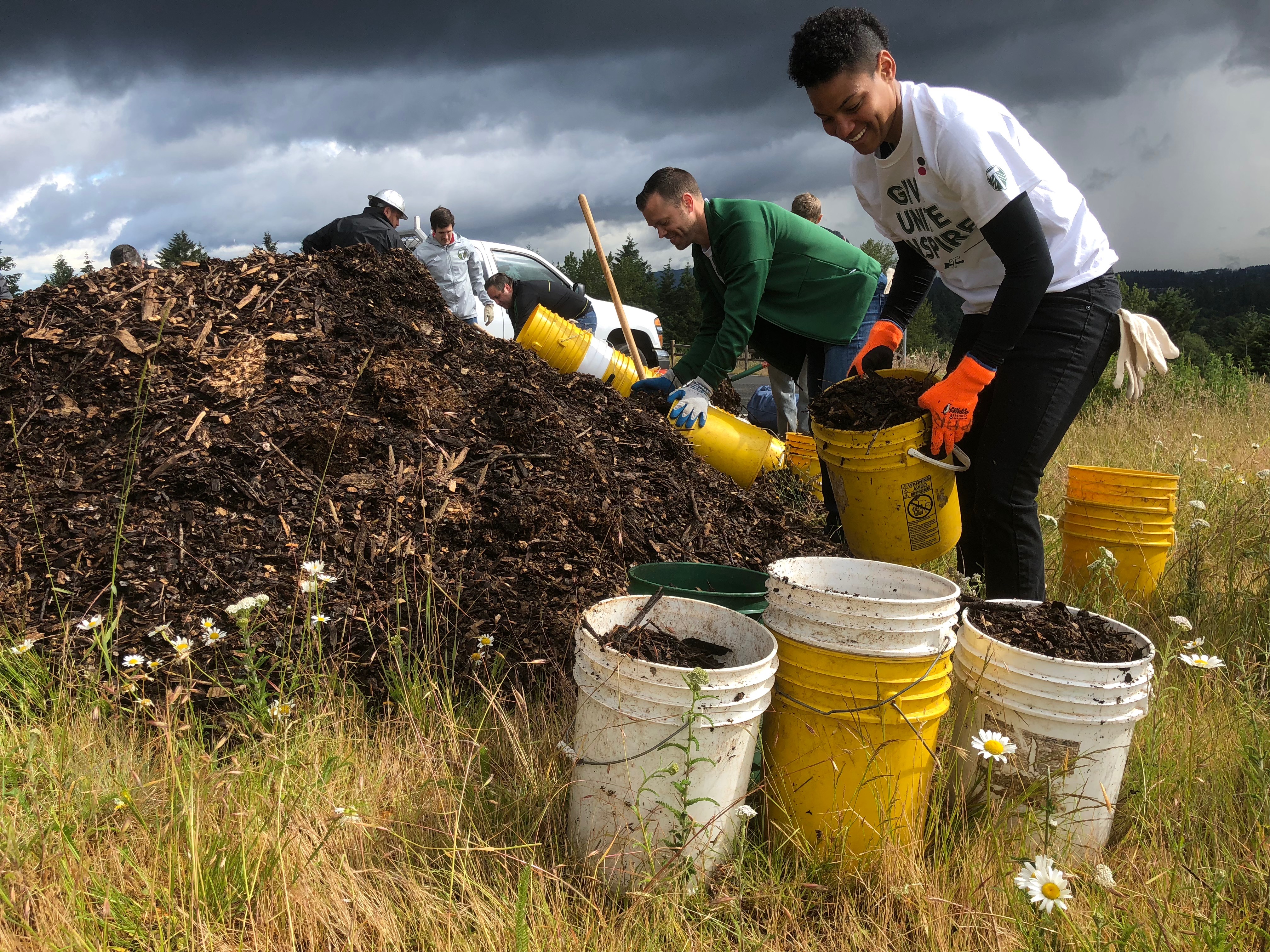 A person holds a bucket of soil next to a pile of soil.