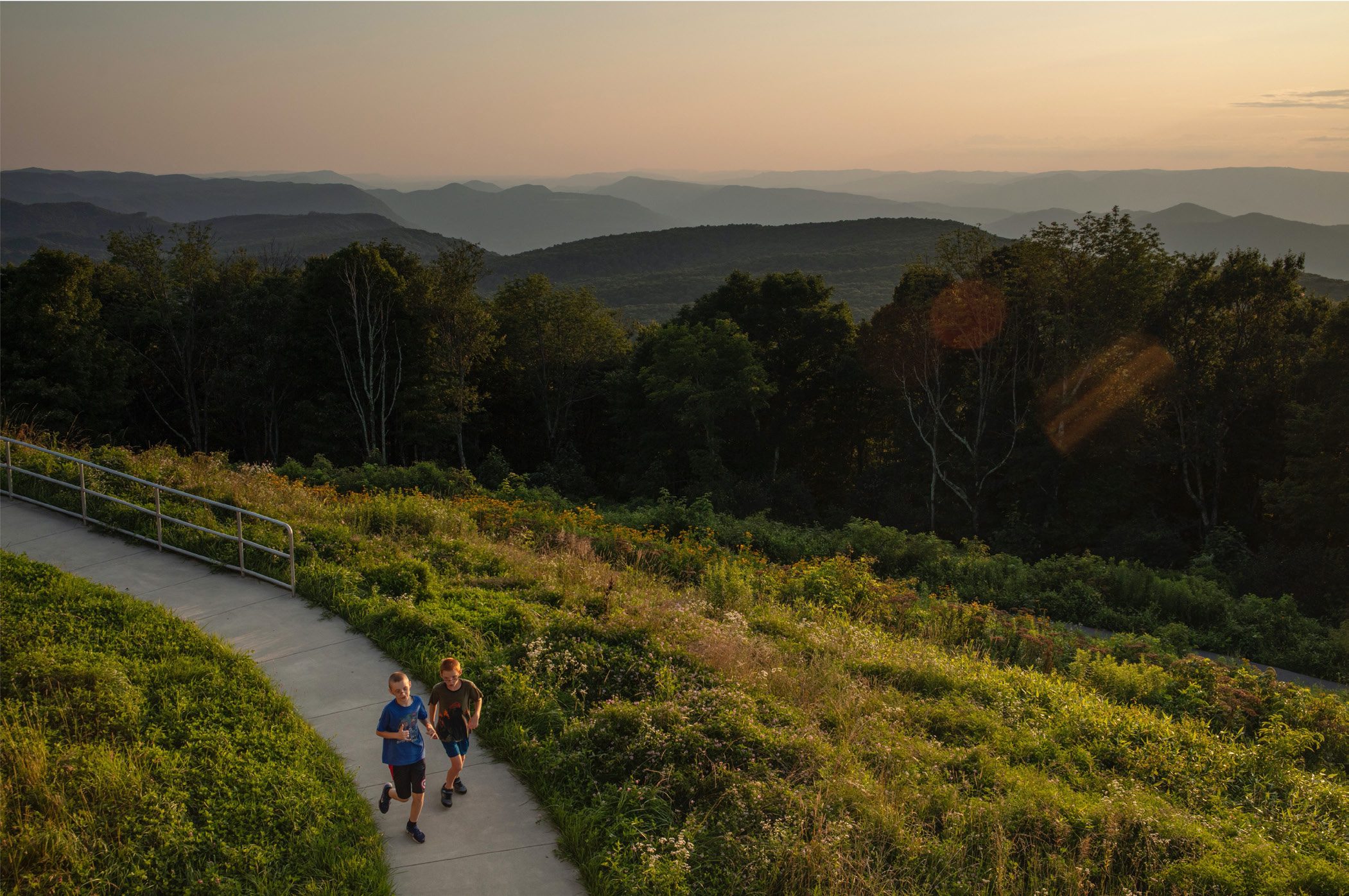 Two children run on a path with a beautiful mountain vista.