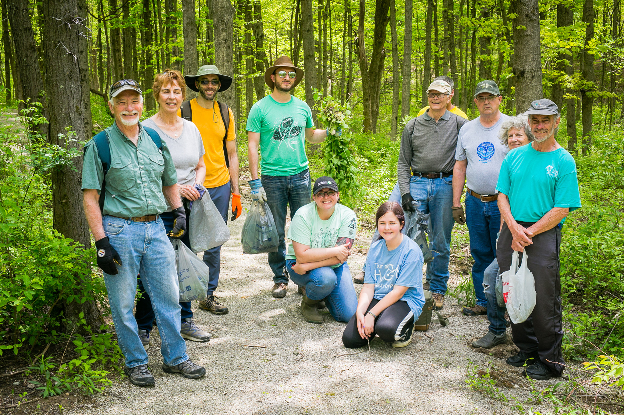 Volunteers hold bags of garlic mustard in forest.