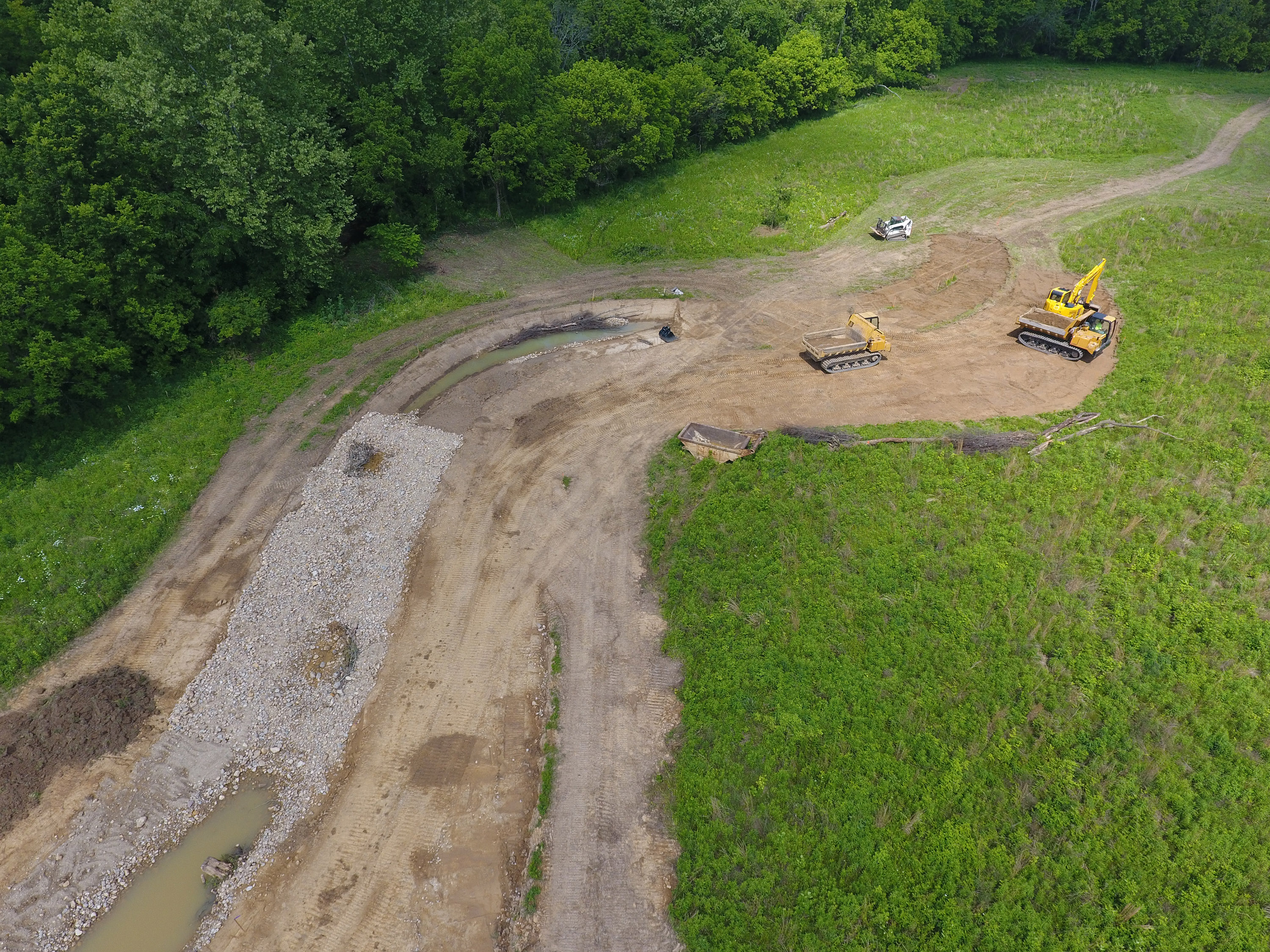 Construction equipment digs up soil around a stream bed.