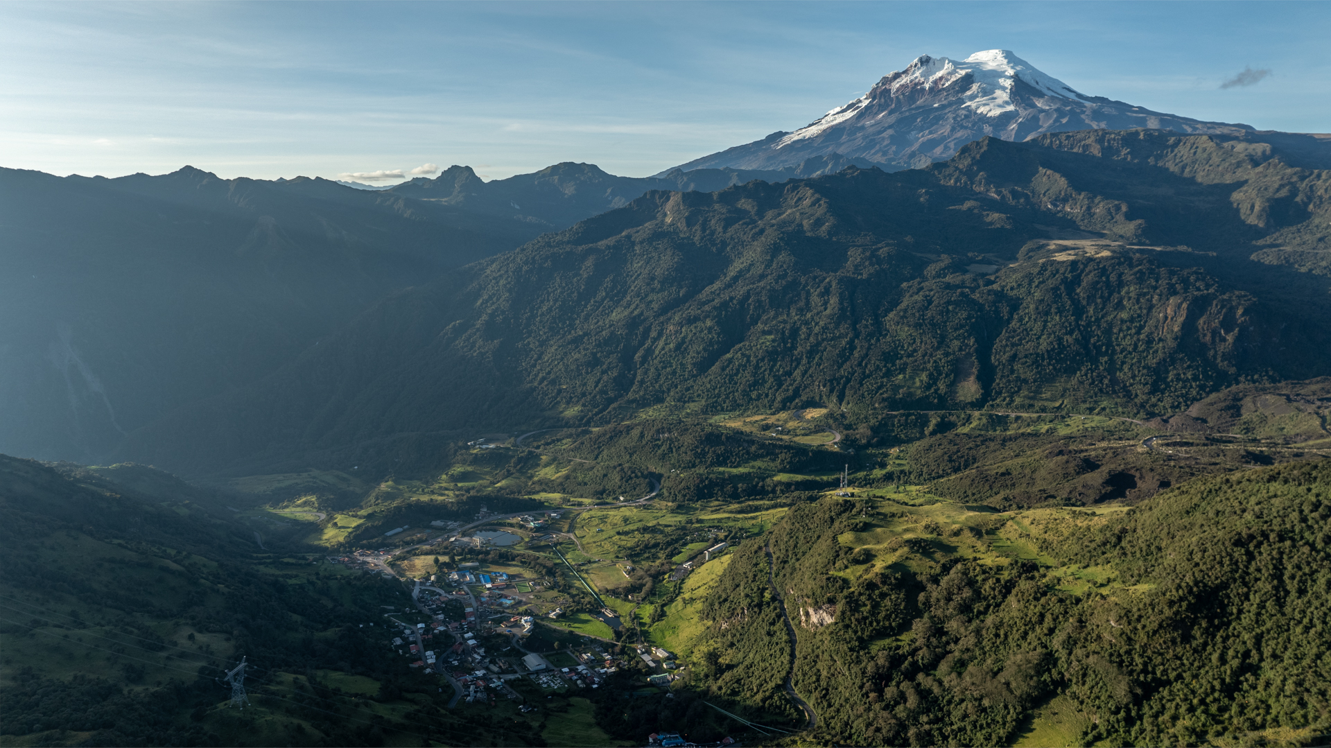 A green field high in a mountainous region, with a snow-capped peak in the background.