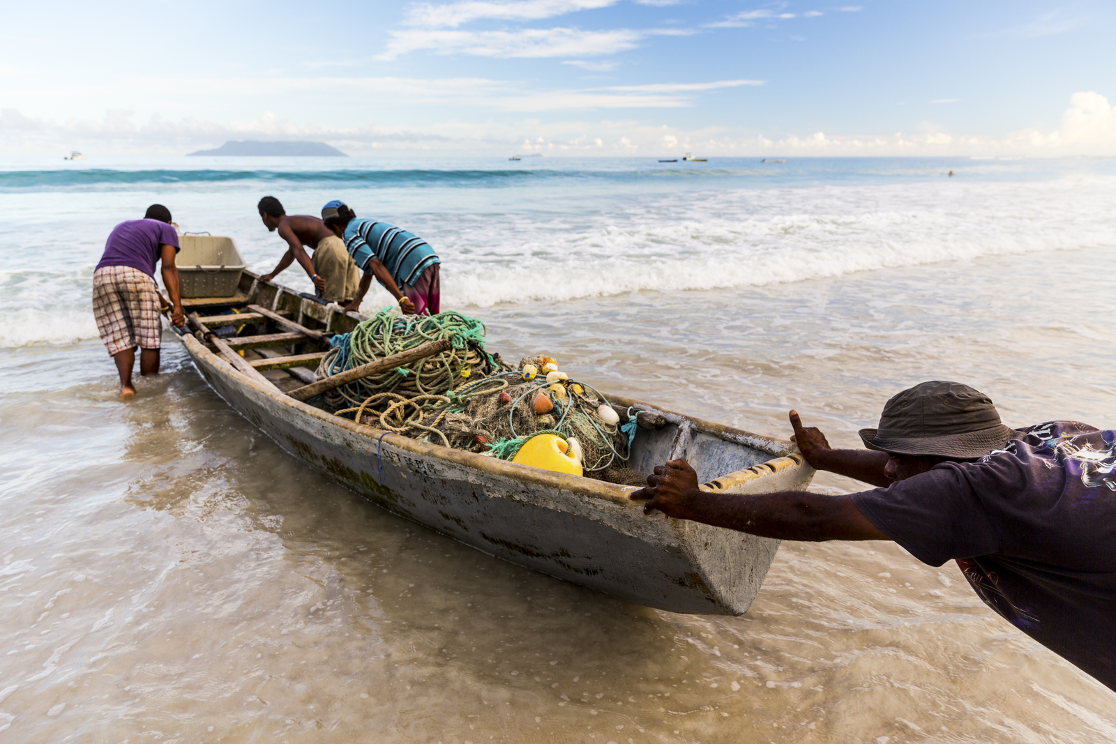 Men pushing a small wooden boat filled with nets.