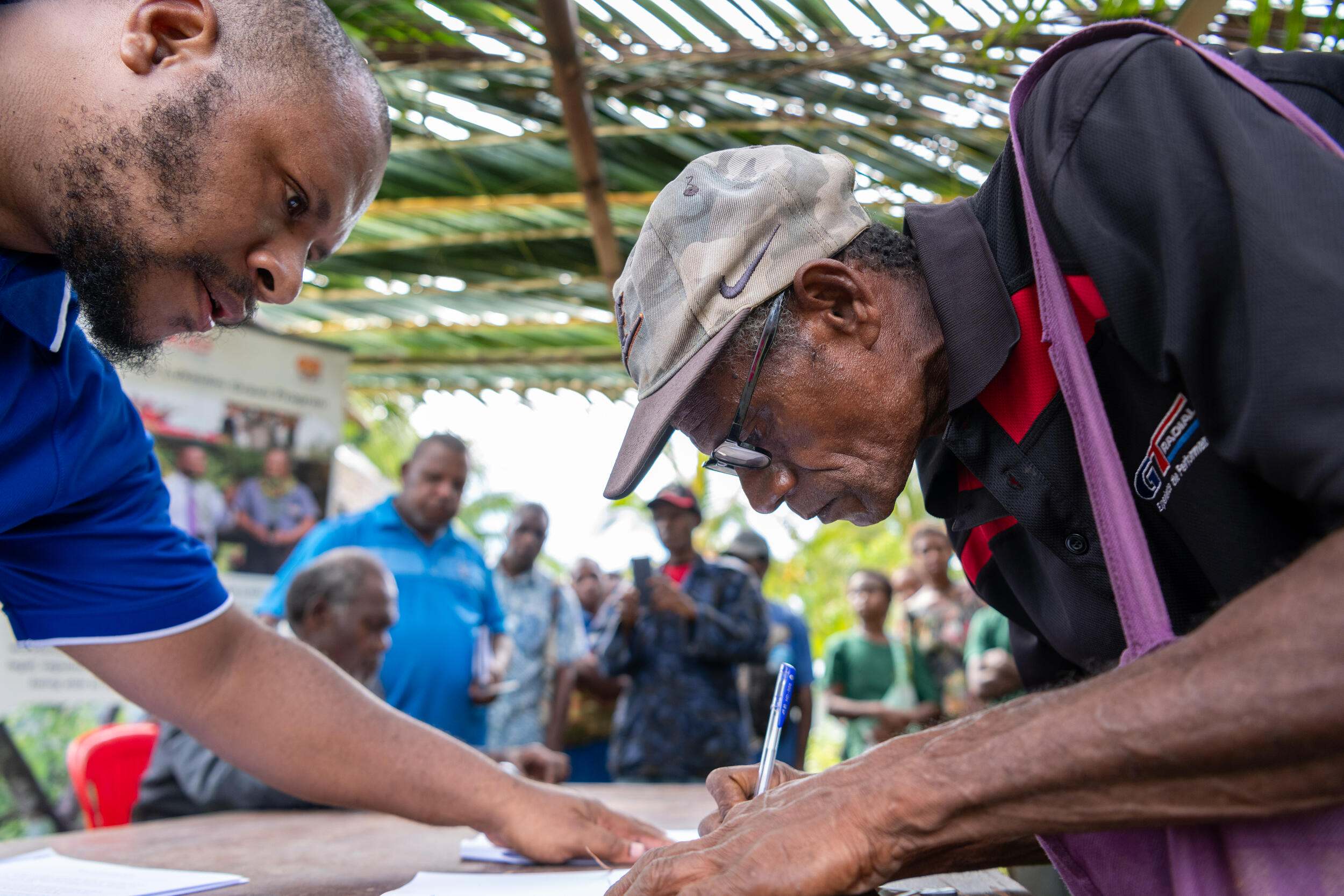 Community member Mathew Lawun is being assisted in signing a document during the CD signing event in the Brem community, Madang Province, Papua New Guinea..