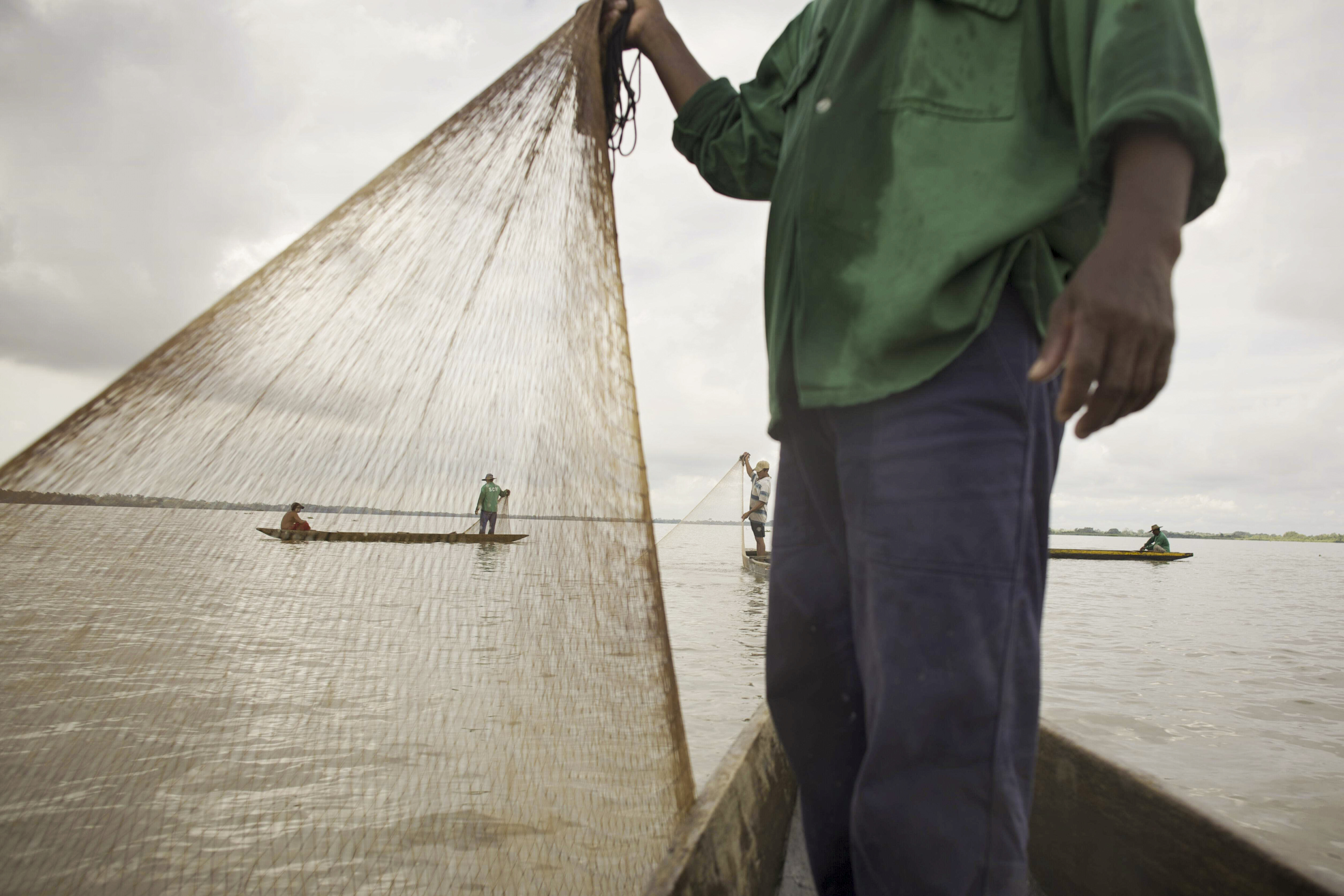  Person holding up a fishing net with boaters and fishermen in the background.