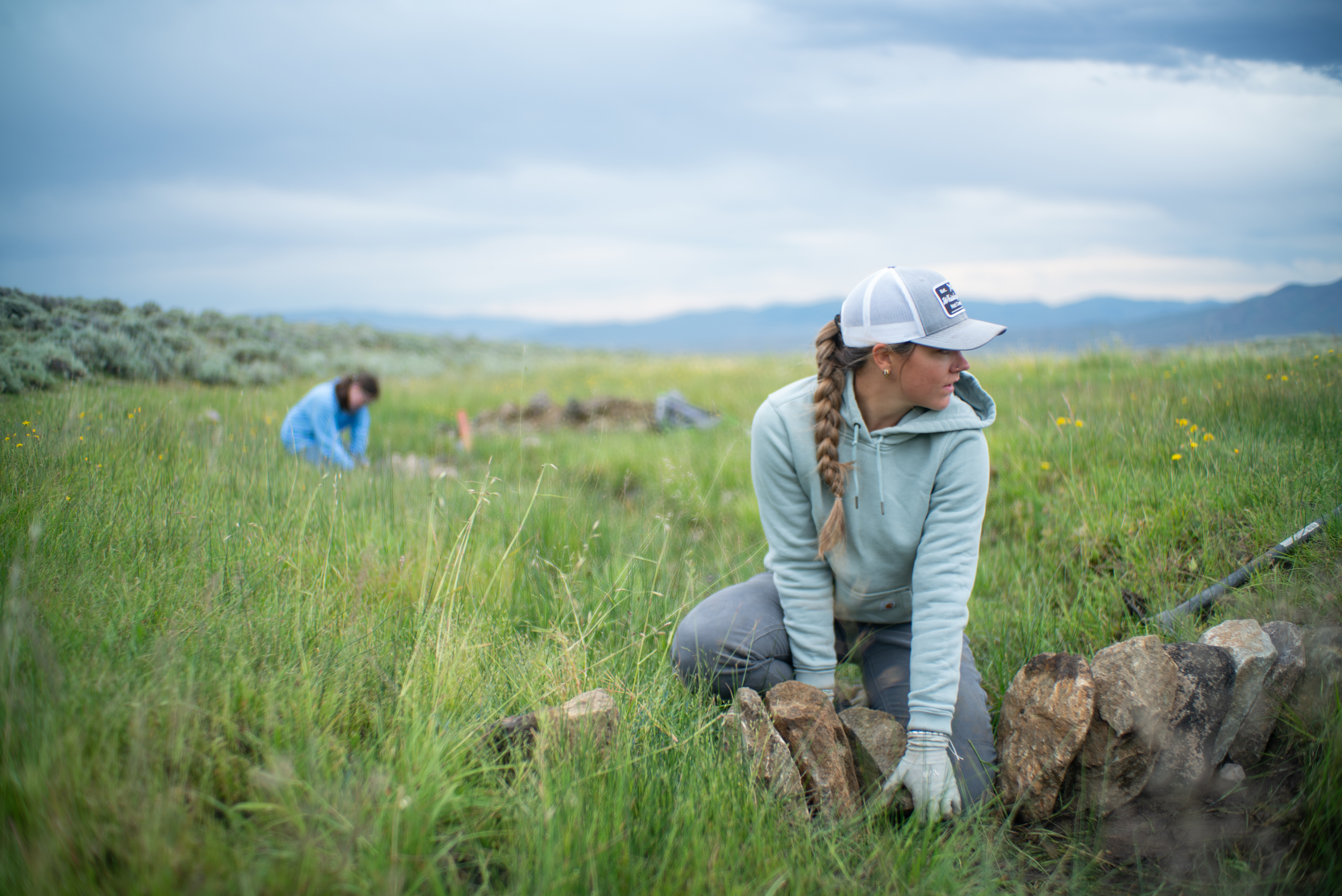 Women with braided hair and hat picks up rock.
