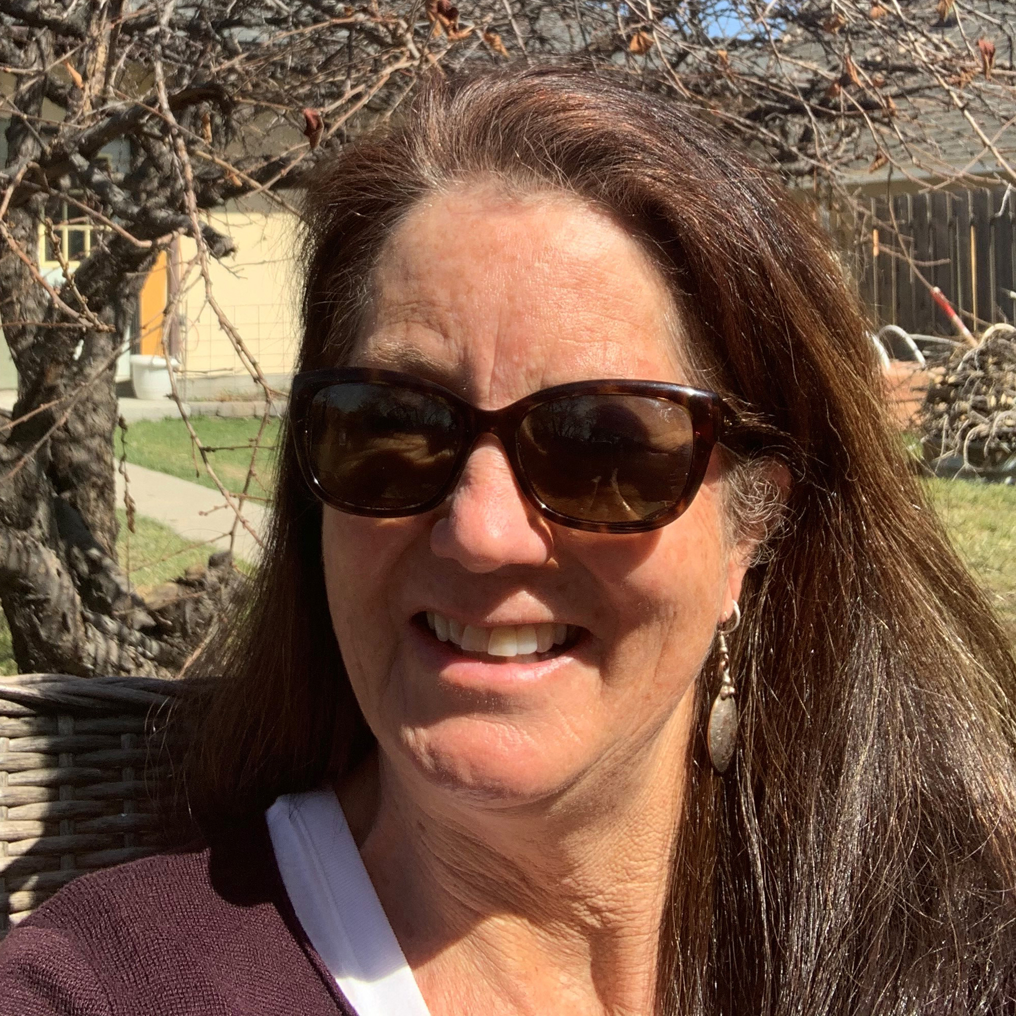 Brunette woman in sunglasses in front of a garden. 