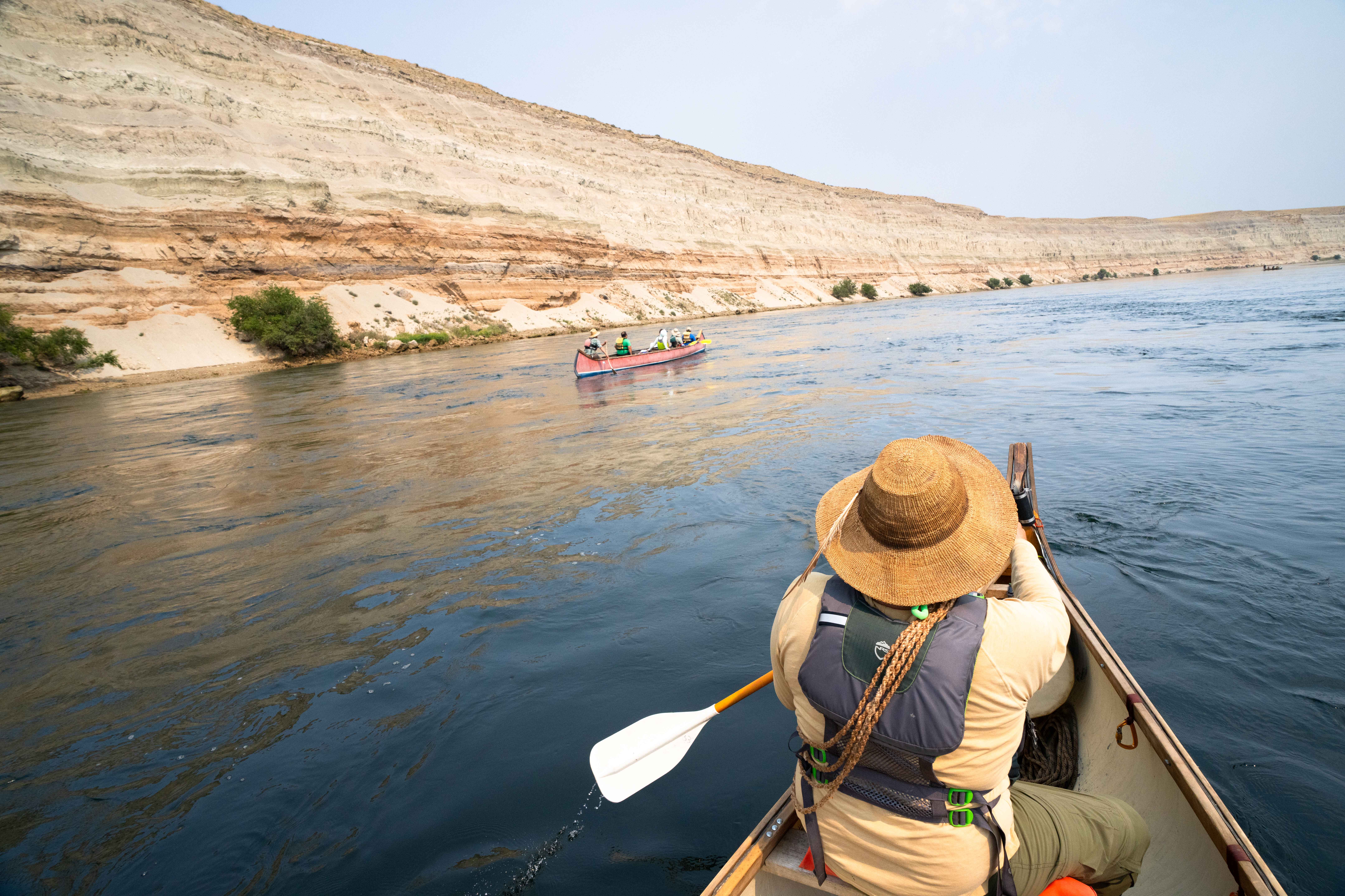 A canoeist, seen from behind, paddles through a river. 