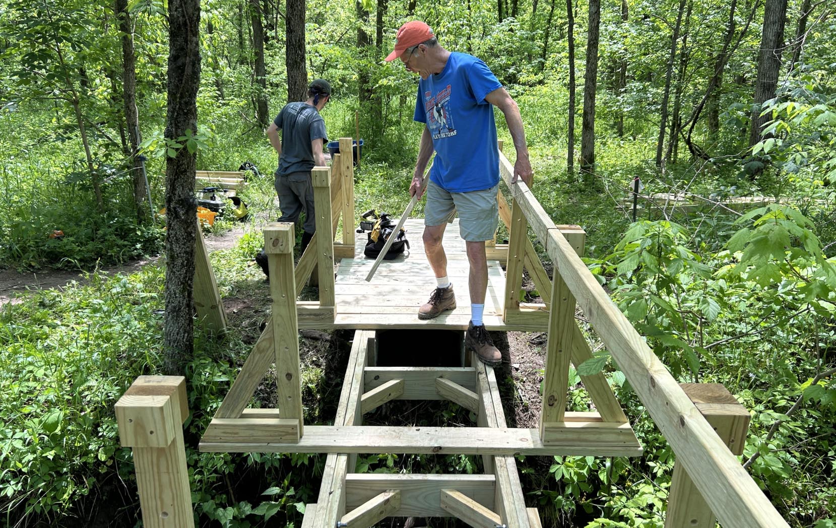 A man helping building a wooden bridge along a path.