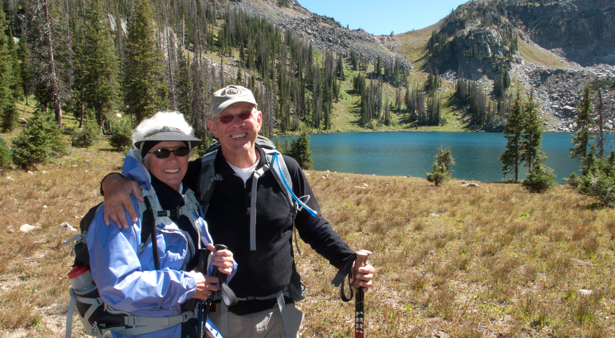 Smiling couple in outdoor gear with hiking poles. 