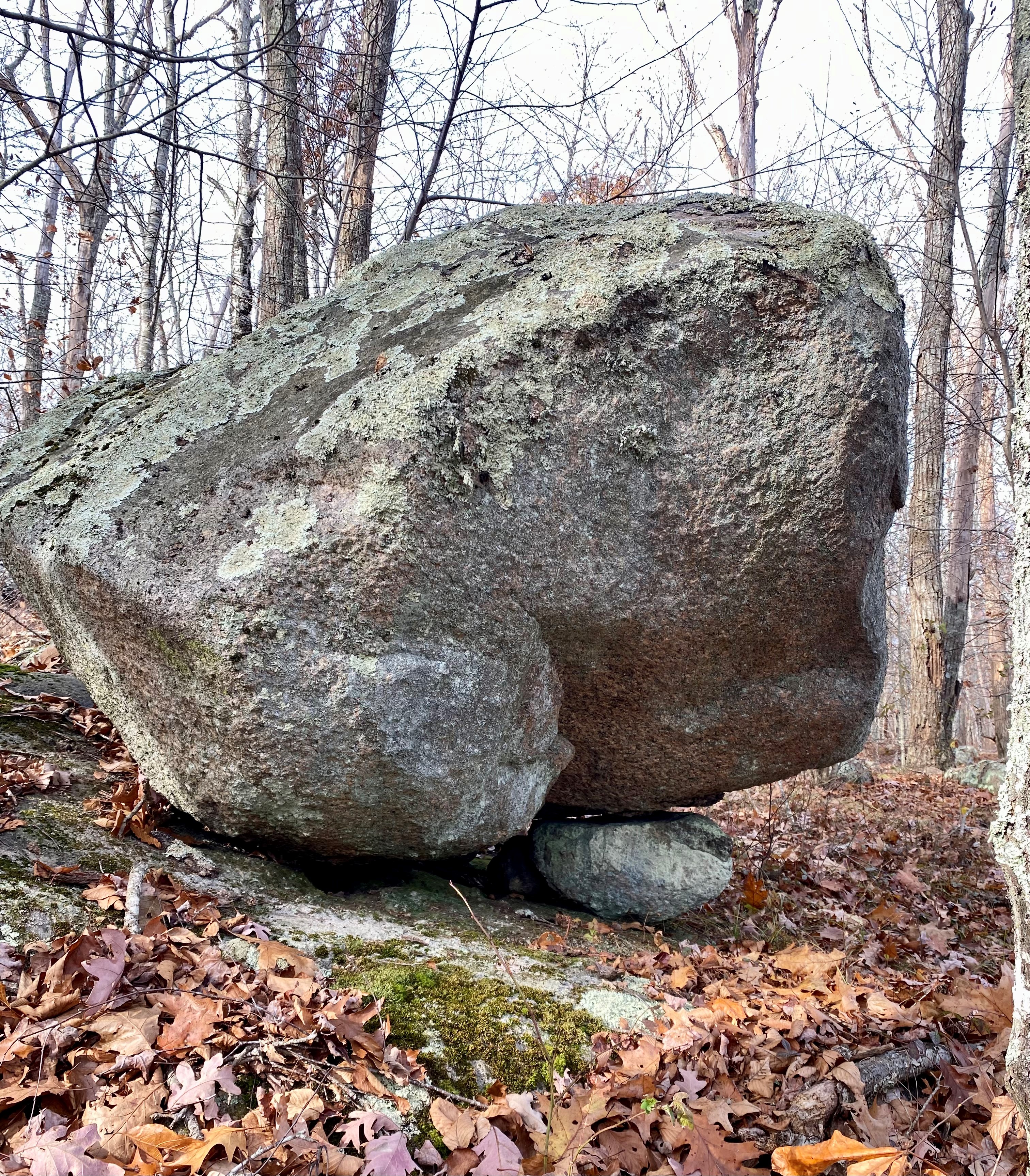 A large gray boulder covered with green lichen, resting on a much smaller stone, tucked underneath at right.