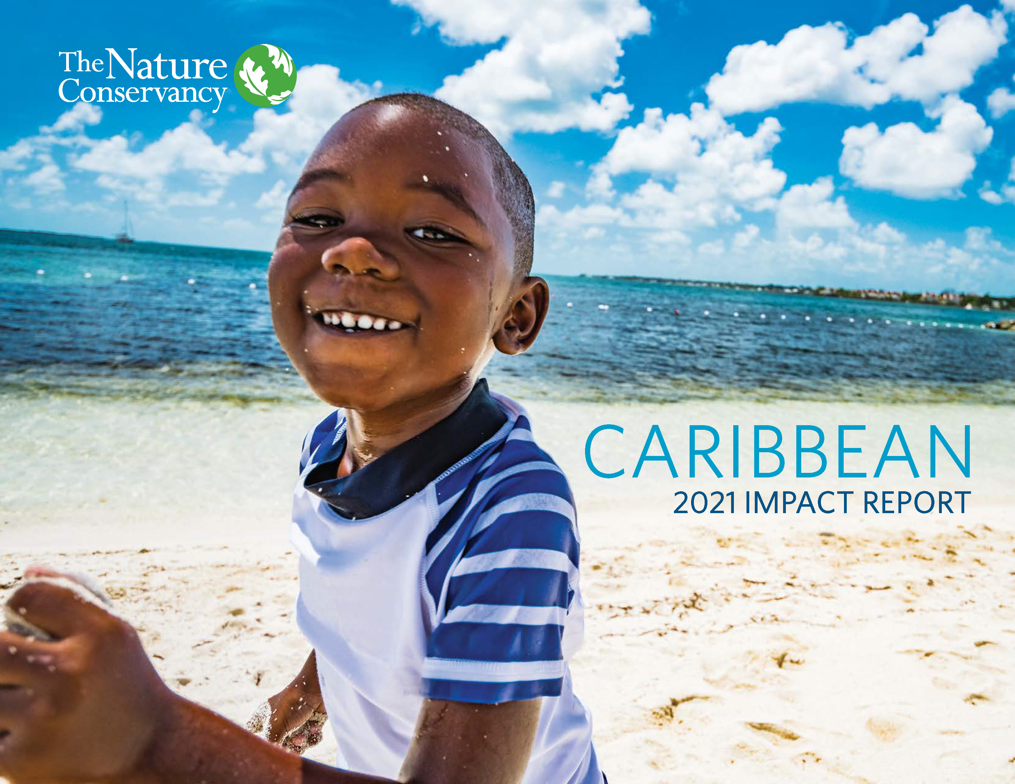 A child smiles on a sandy beach with blue ocean beyond.