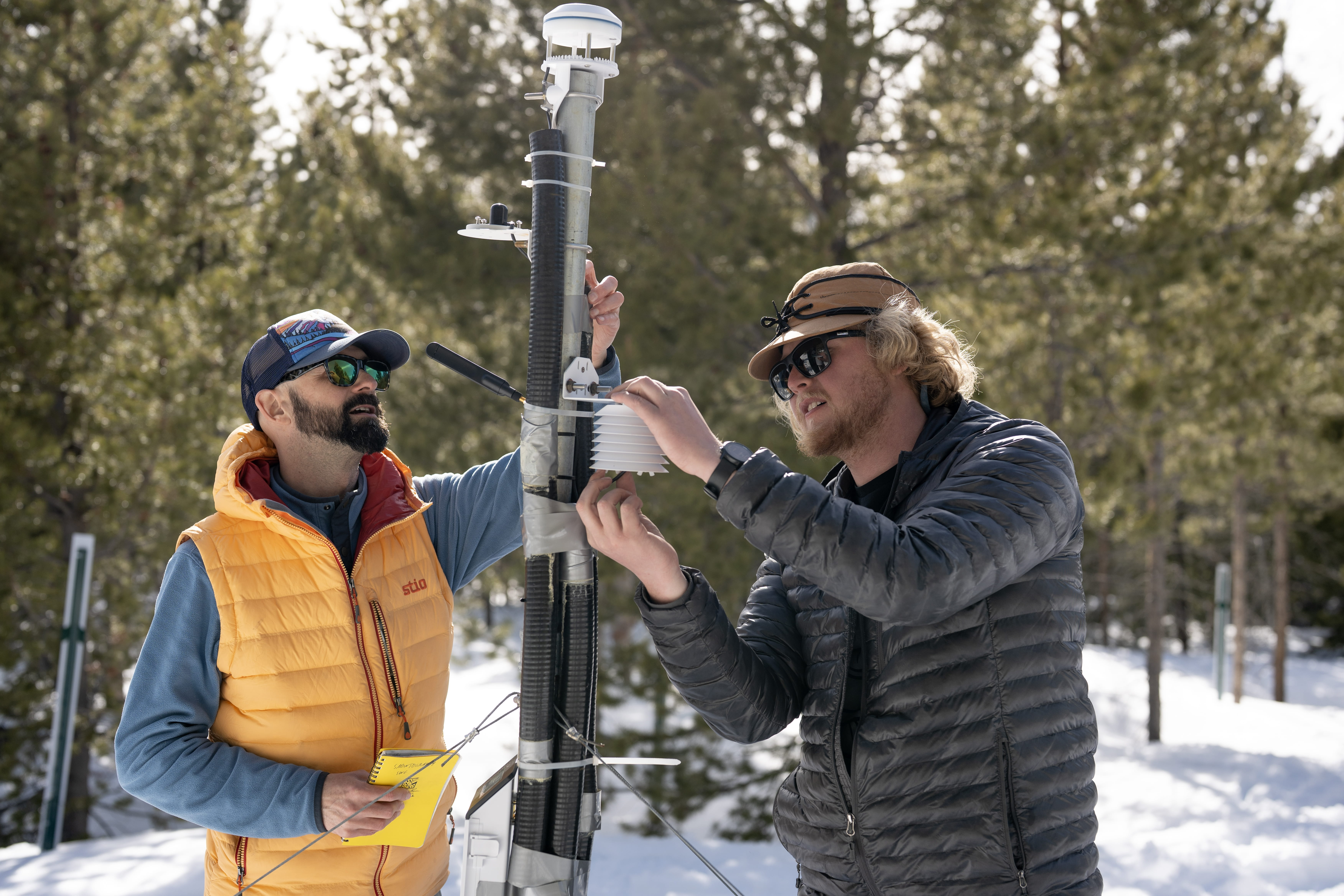 Two people measure snow with a ruler.