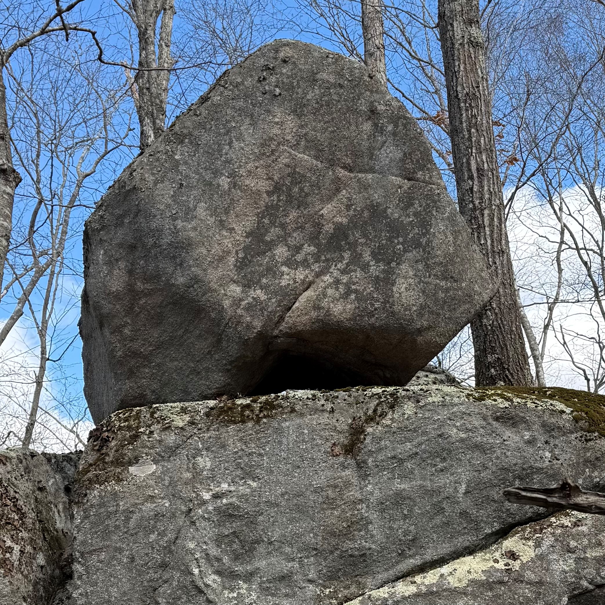 A round, gray boulder sits on a flat outcropping of gray granite against a clear blue sky.