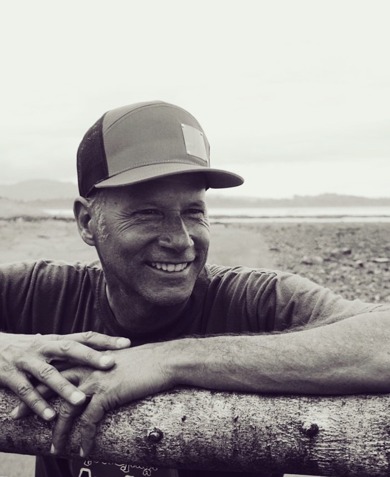 Sepia photo of smiling man in cap, leaning on fence.