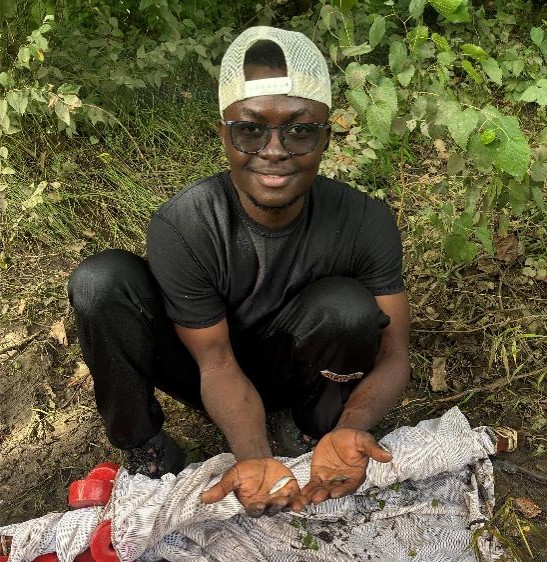 A man in a backwards hat holds a small fish in his hand.