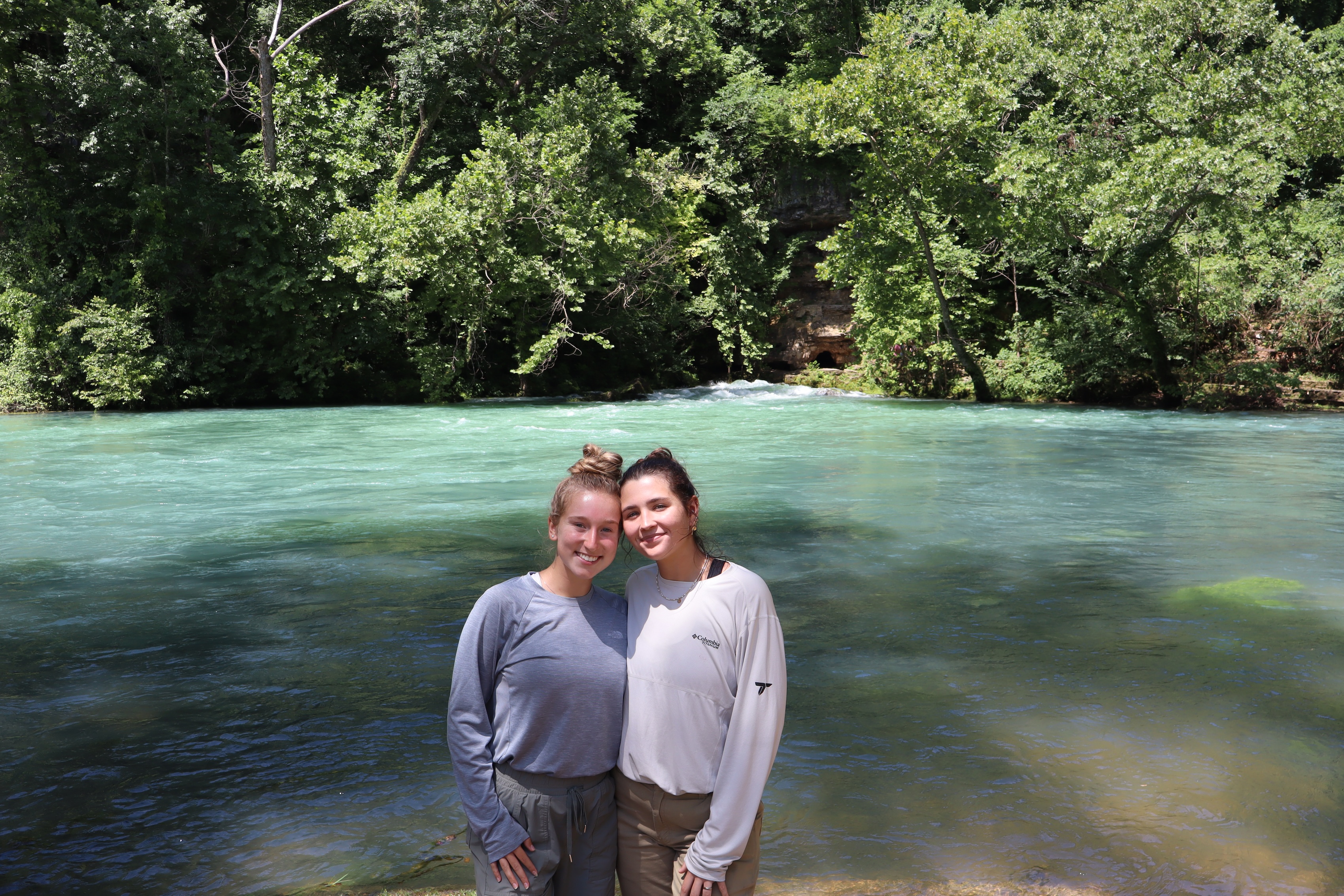 Two women stand in front of a river.