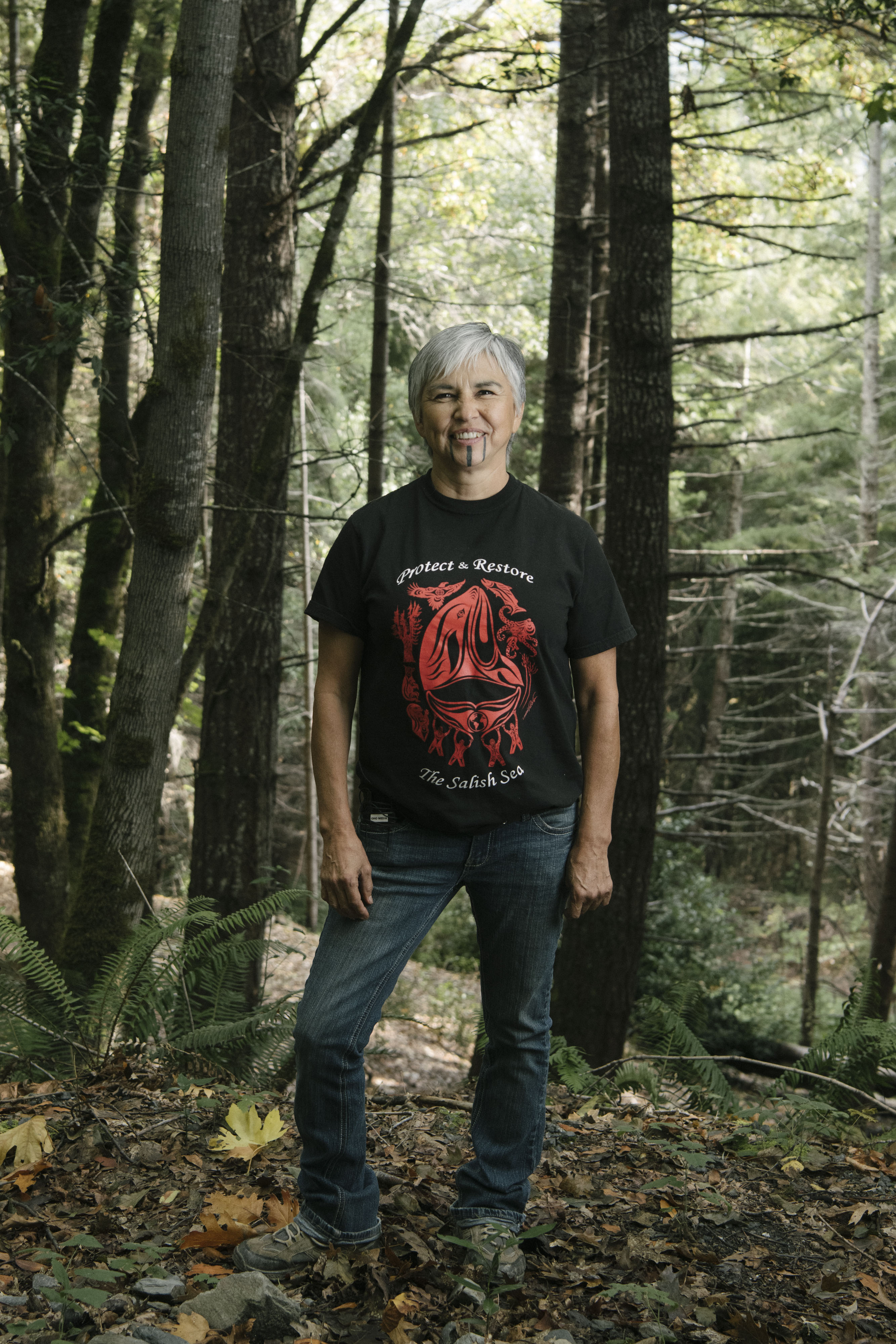 Woman in black t-shirt stands in forest.