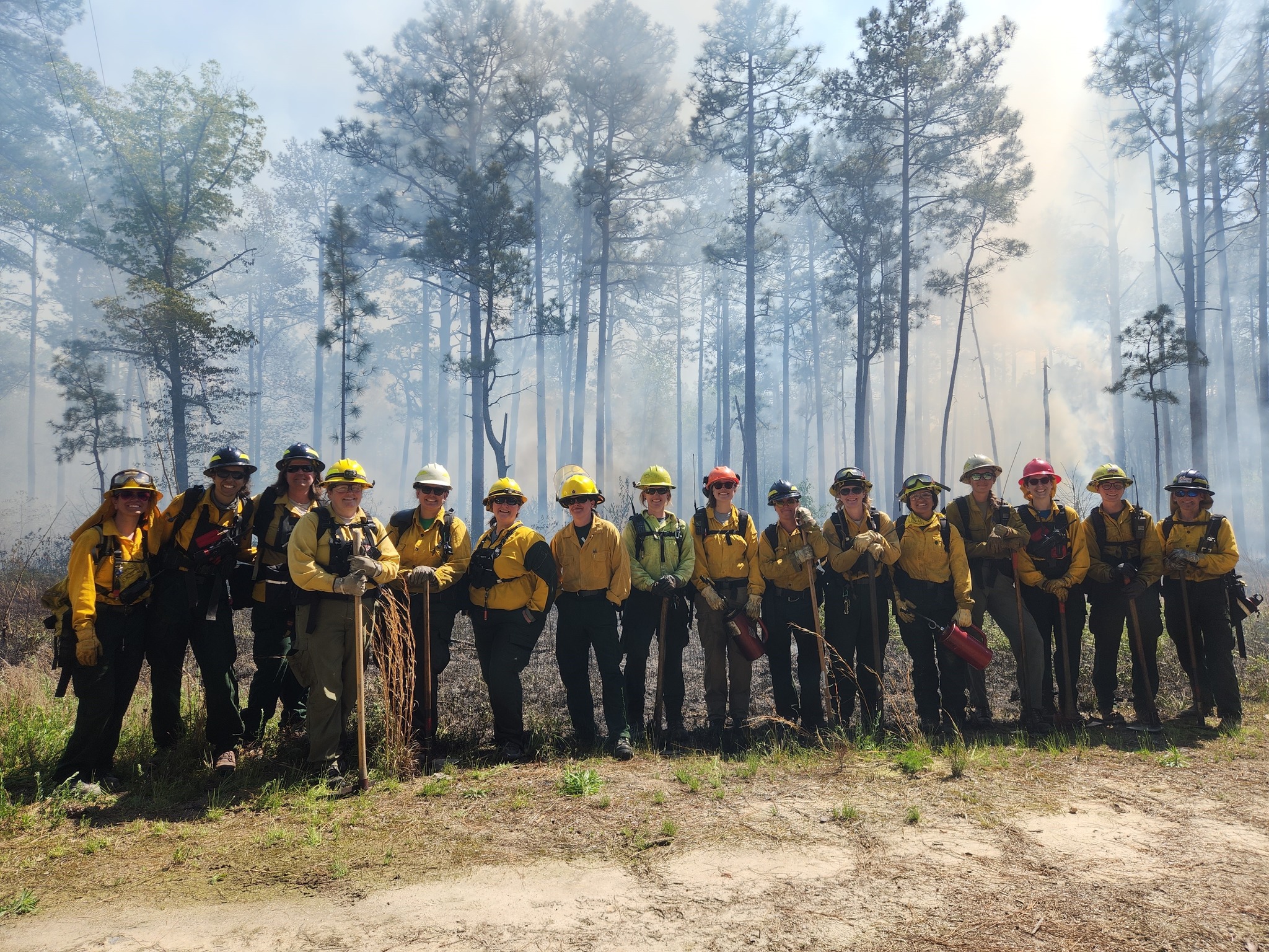 A group of fire practioners pose together in a line during a controlled burn.