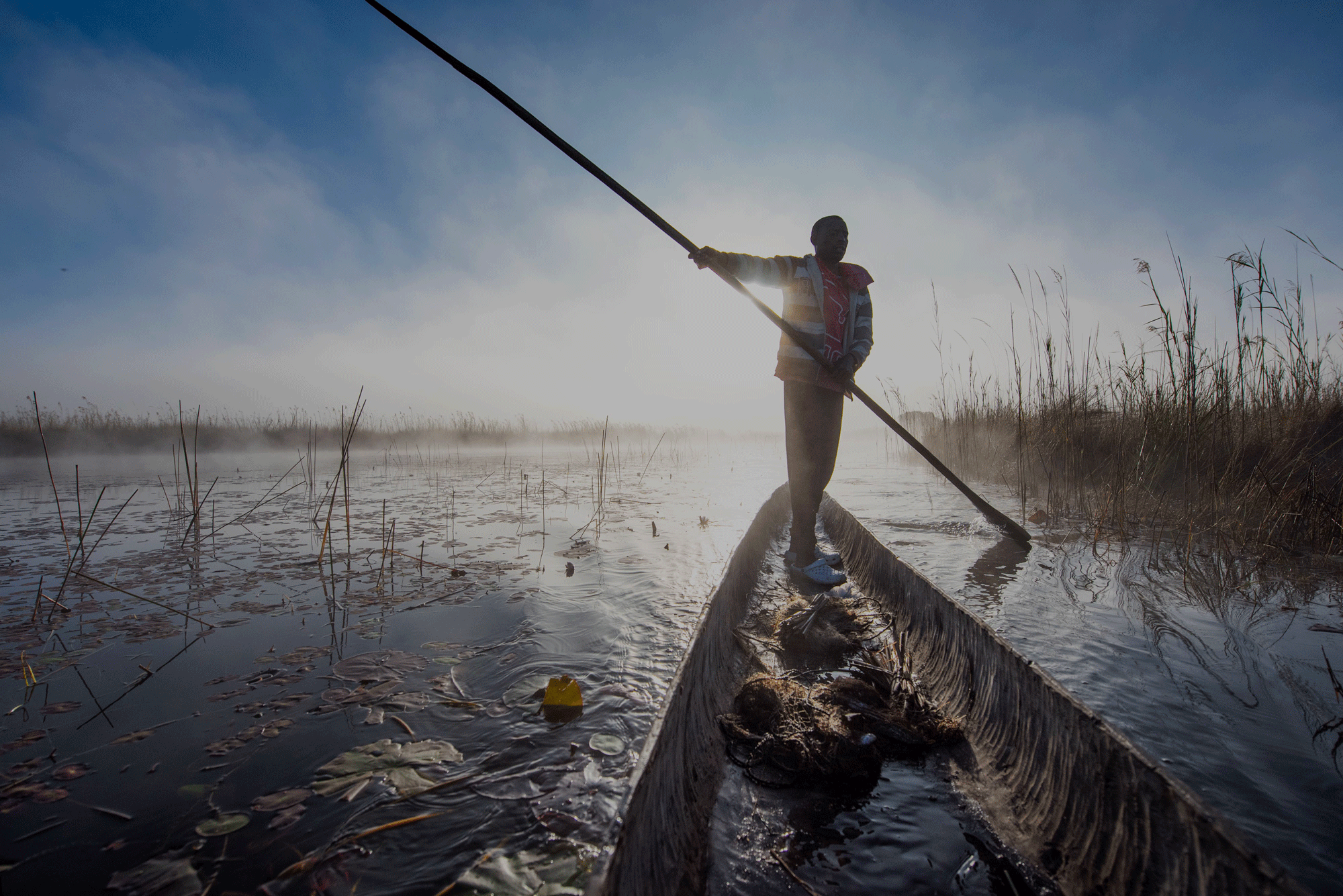 A person standing with a long oar paddles through Botswana's iconic Okavango Delta.