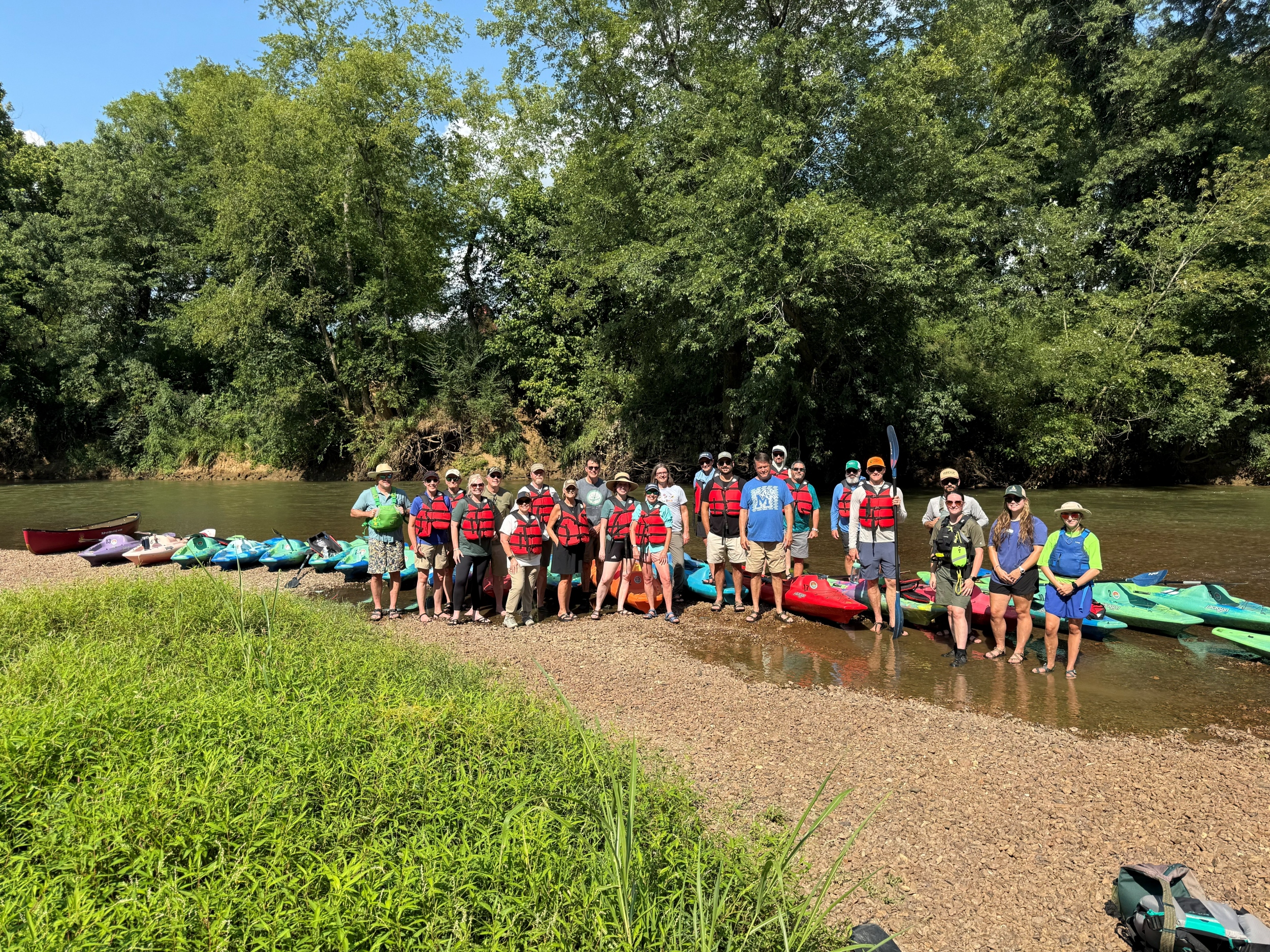 A group of conservation leaders wearing life jackets and standing in a river with kayaks around them.