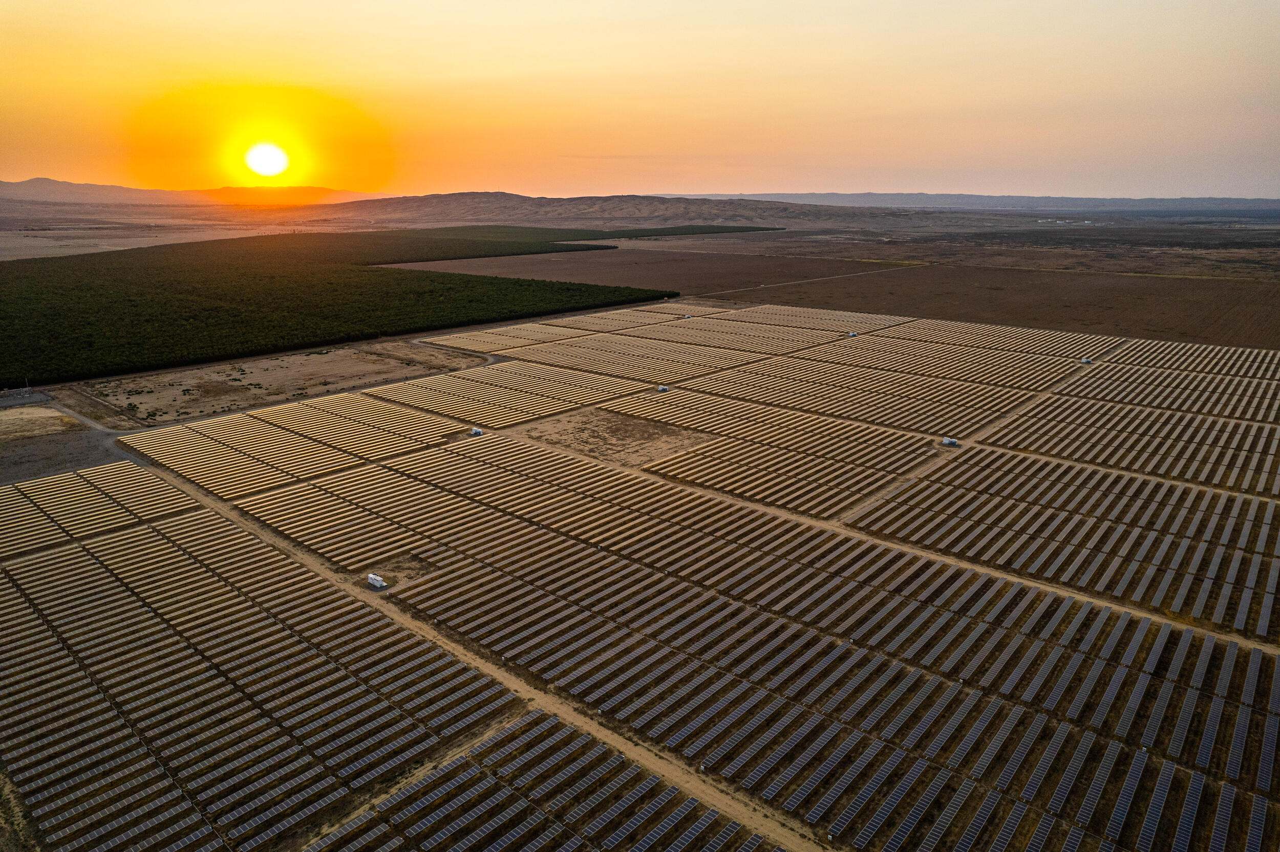 The sun sets over a wide expanse of farm land.