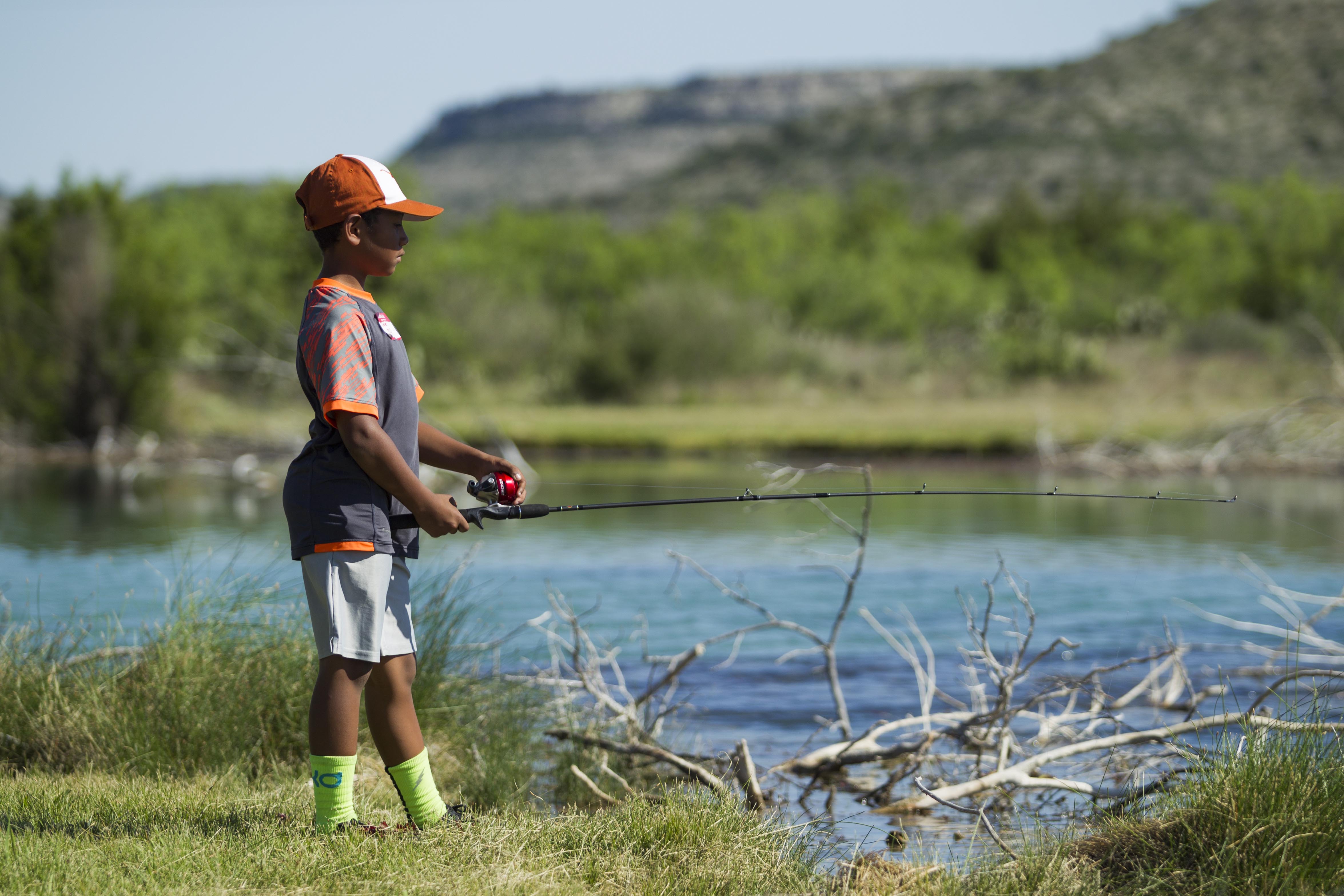 A boy holds a fishing rod as he stands near a creek.