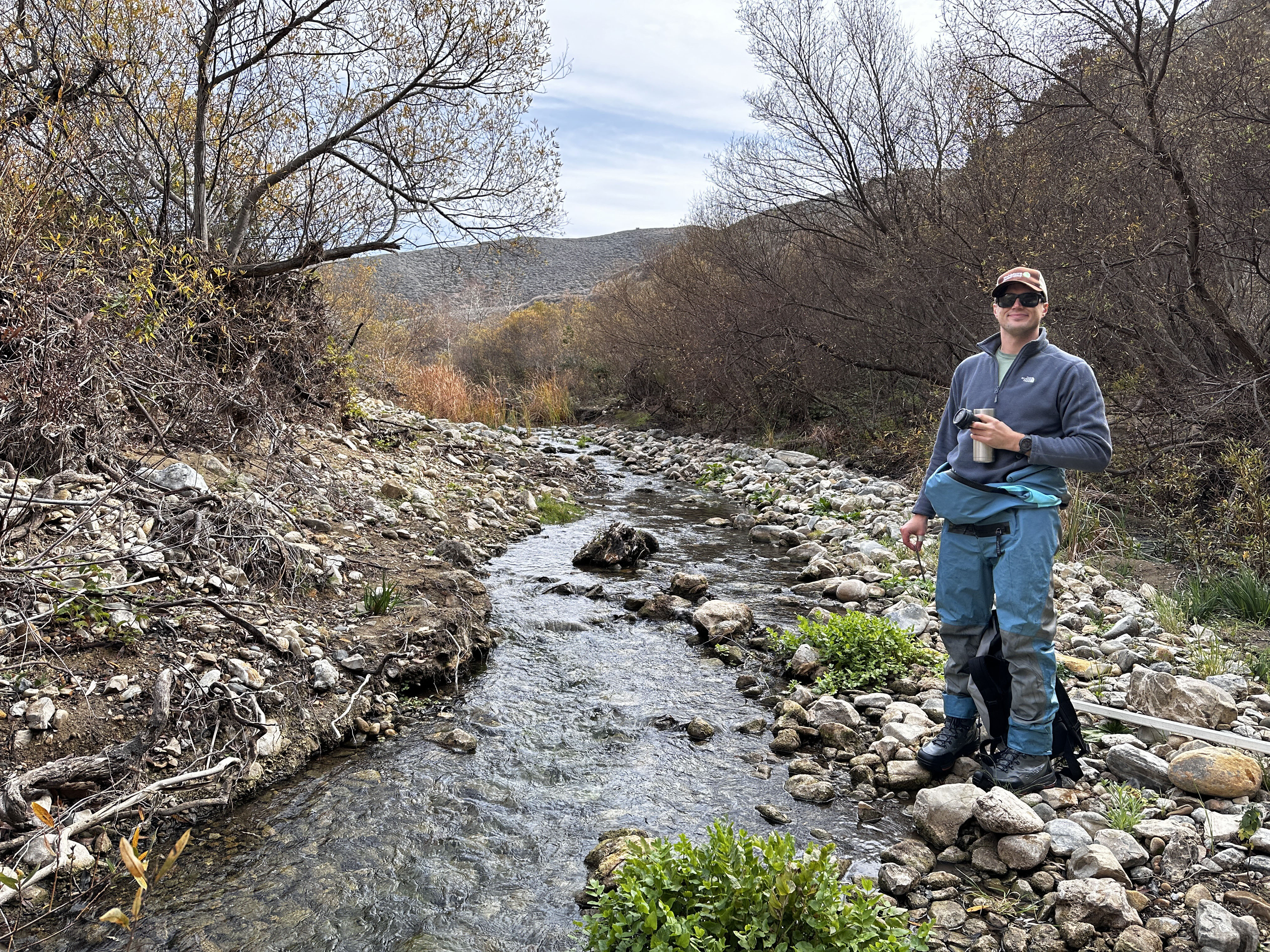 A man stands next to a small flowing creek. 