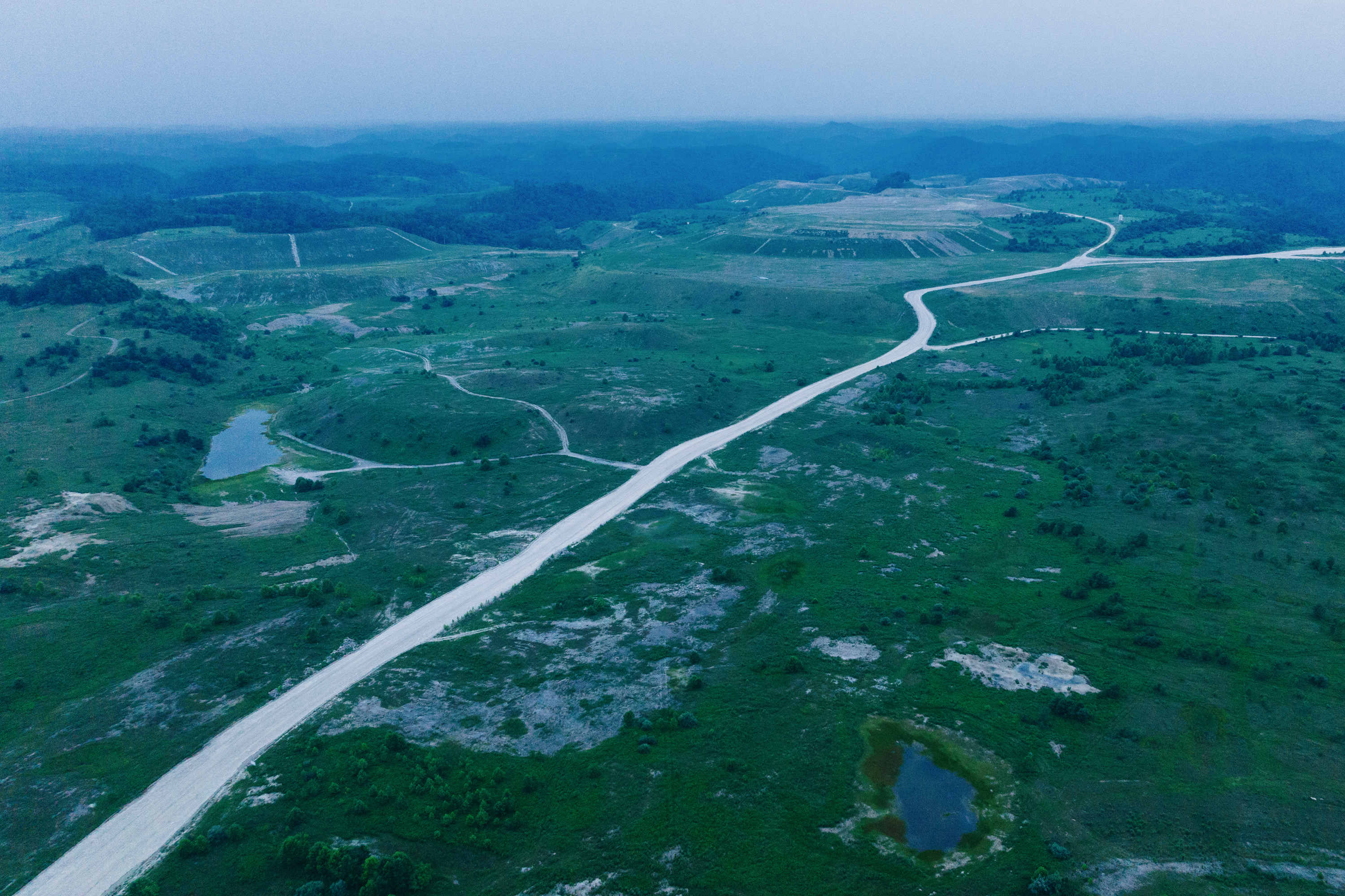 An aerial image over a green landscape with a road running through it.