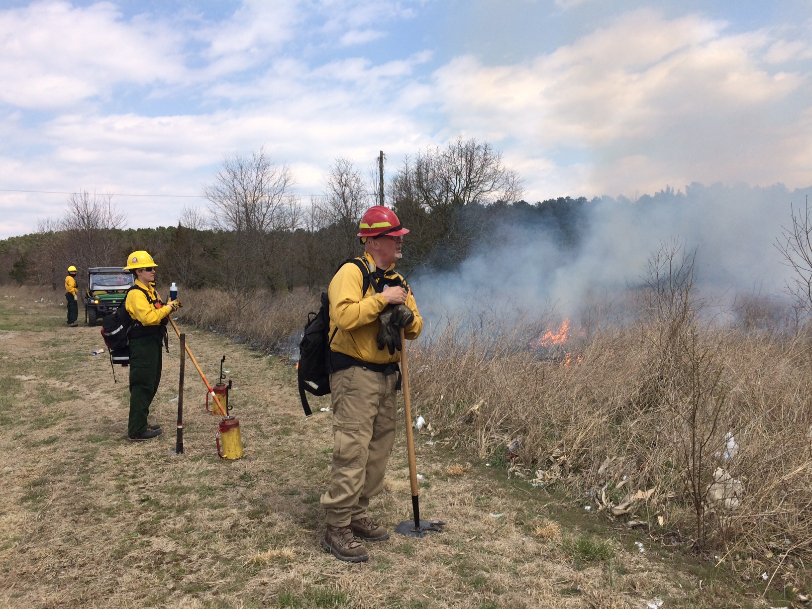 Two people wearing yellow fire gear monitor a burn.