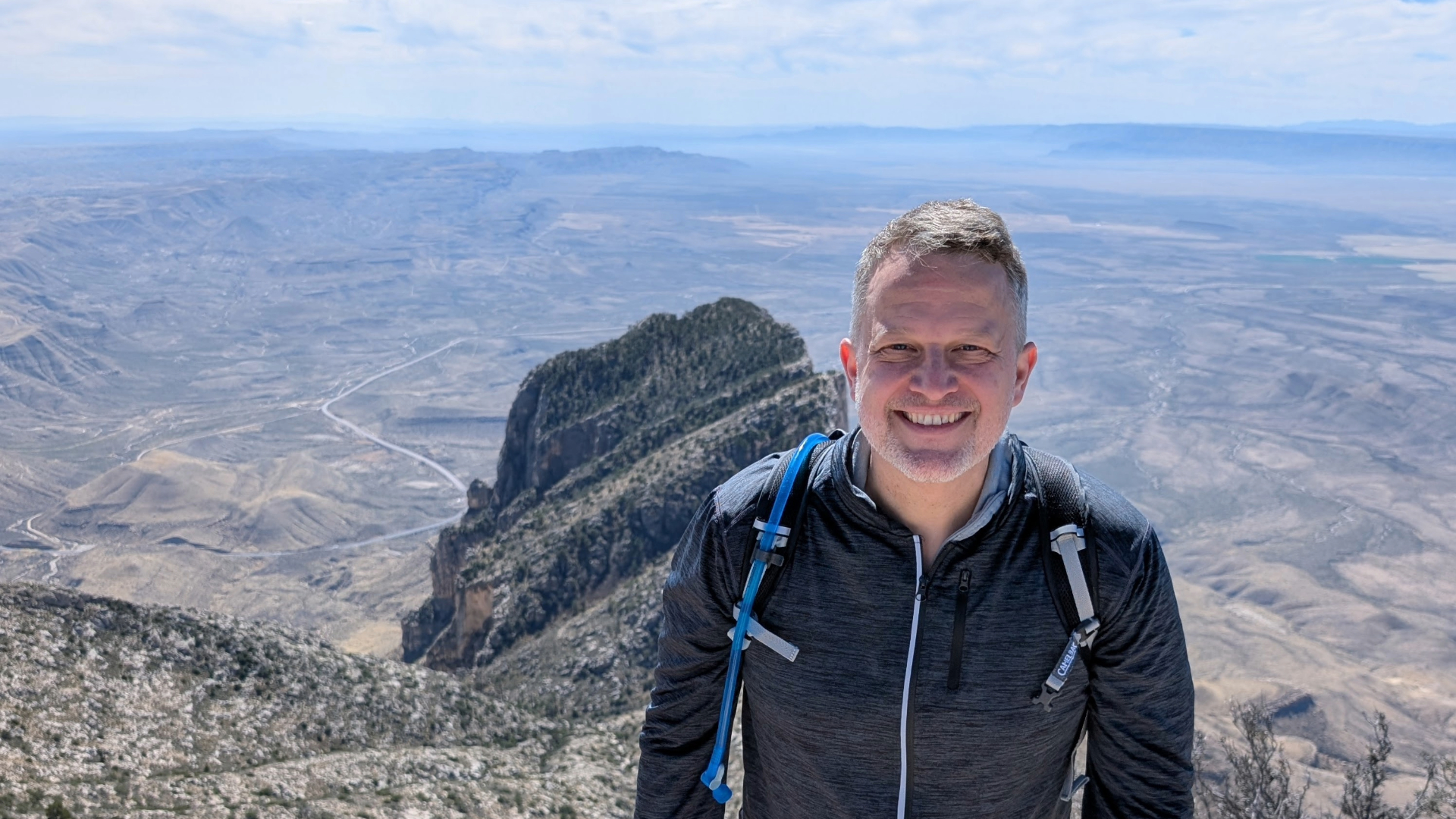 James McGuire stands in front of sweeping mountains and canyons dotted with brush.