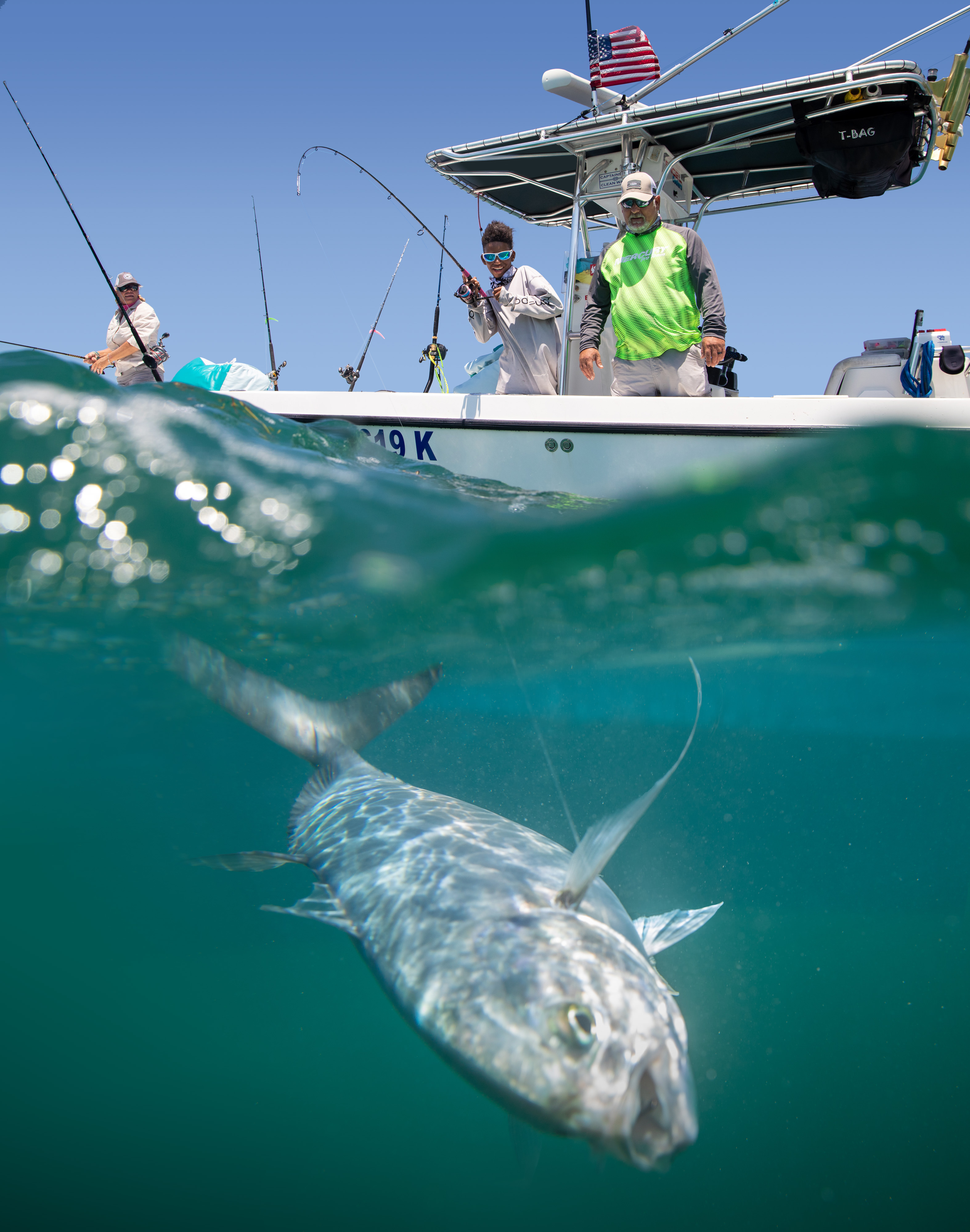 Half underwater, half above water view of a fish and people on a boat above fishing.