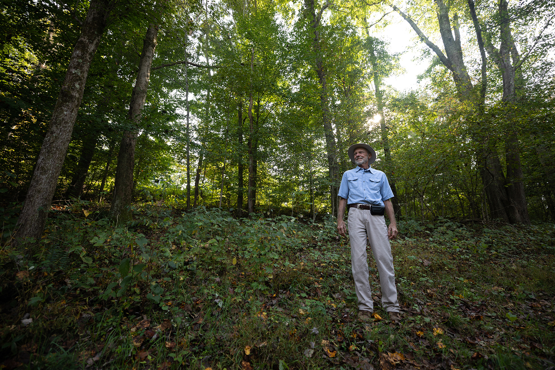 Jerry Long, in khakis and blue shirt, stands in forest.