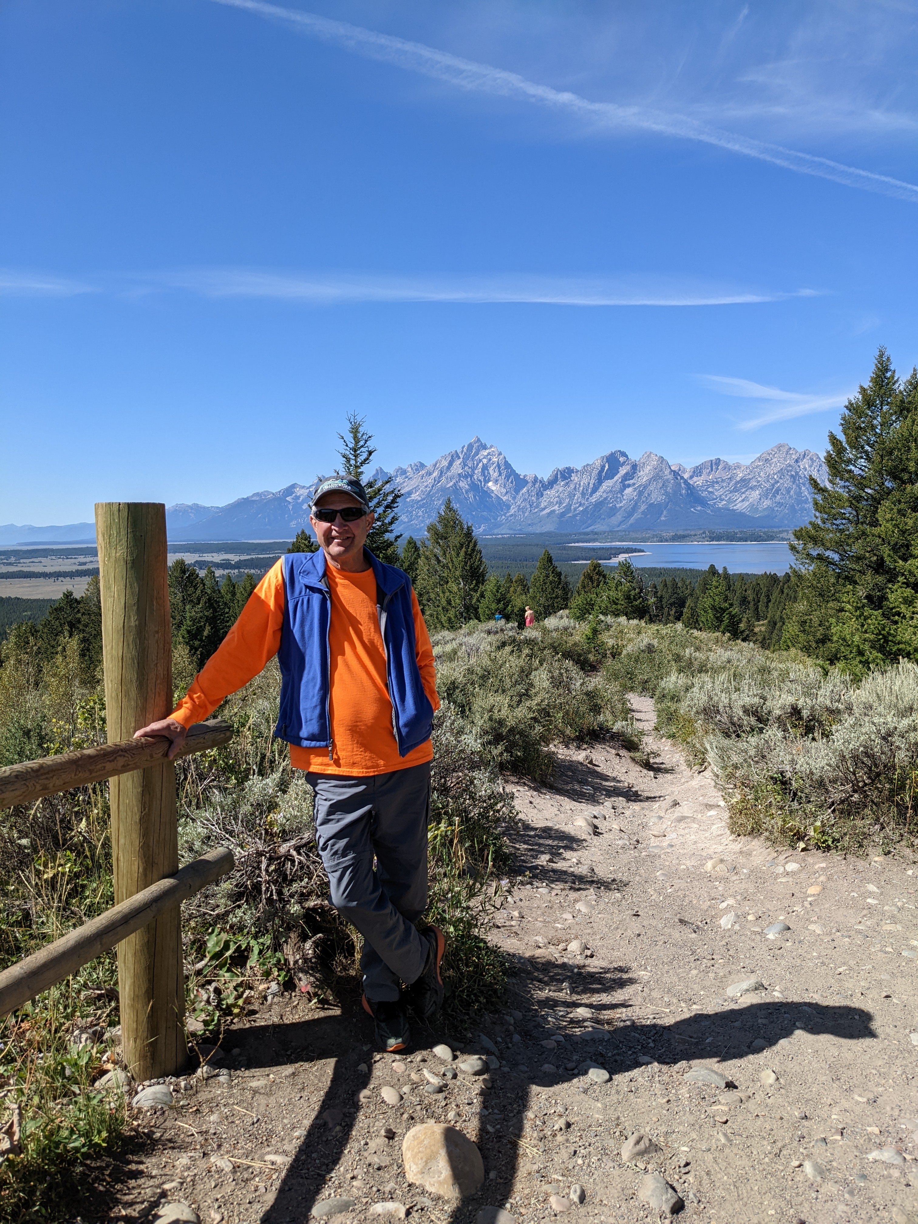 A man leans on a fence in front of a mountain range.