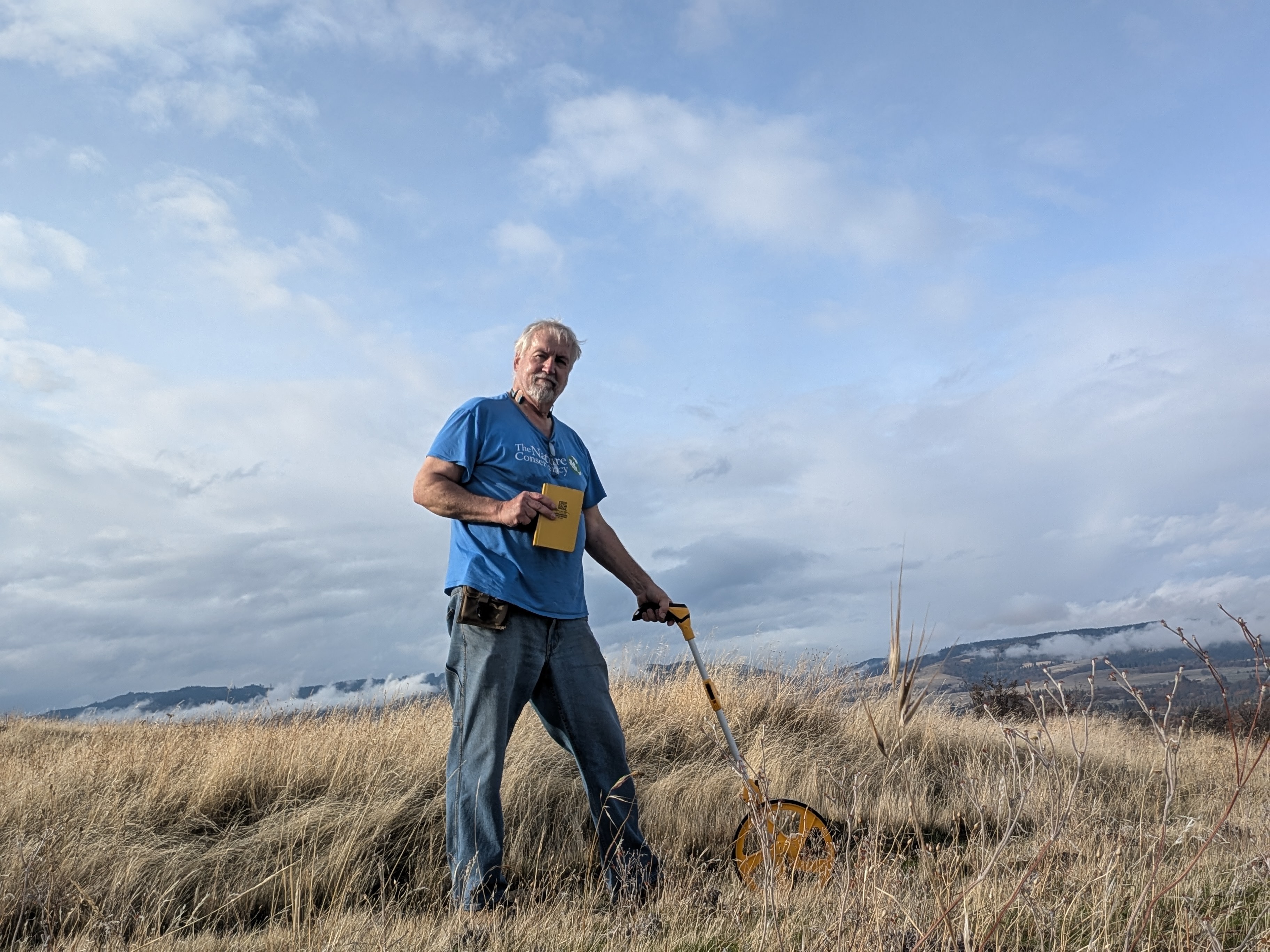 Man stands in grassy field with notebook and science equipment.