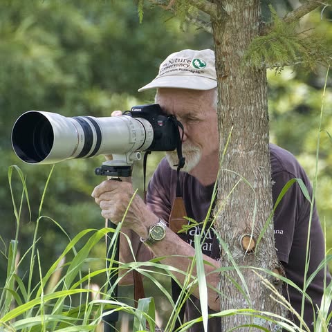 A man wearing a hat looks through a large camera lens.