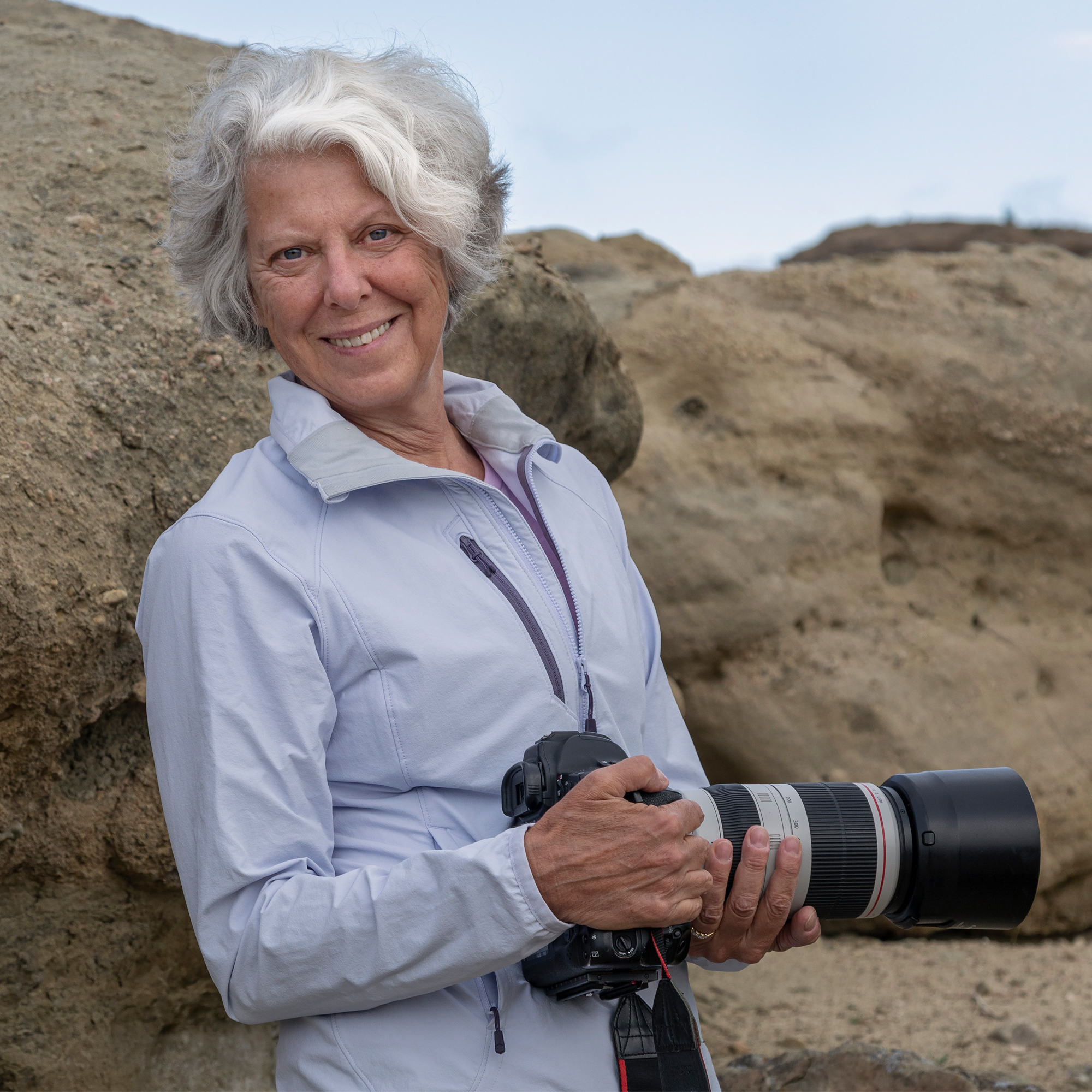 A woman facing forward and holding a large camera. 