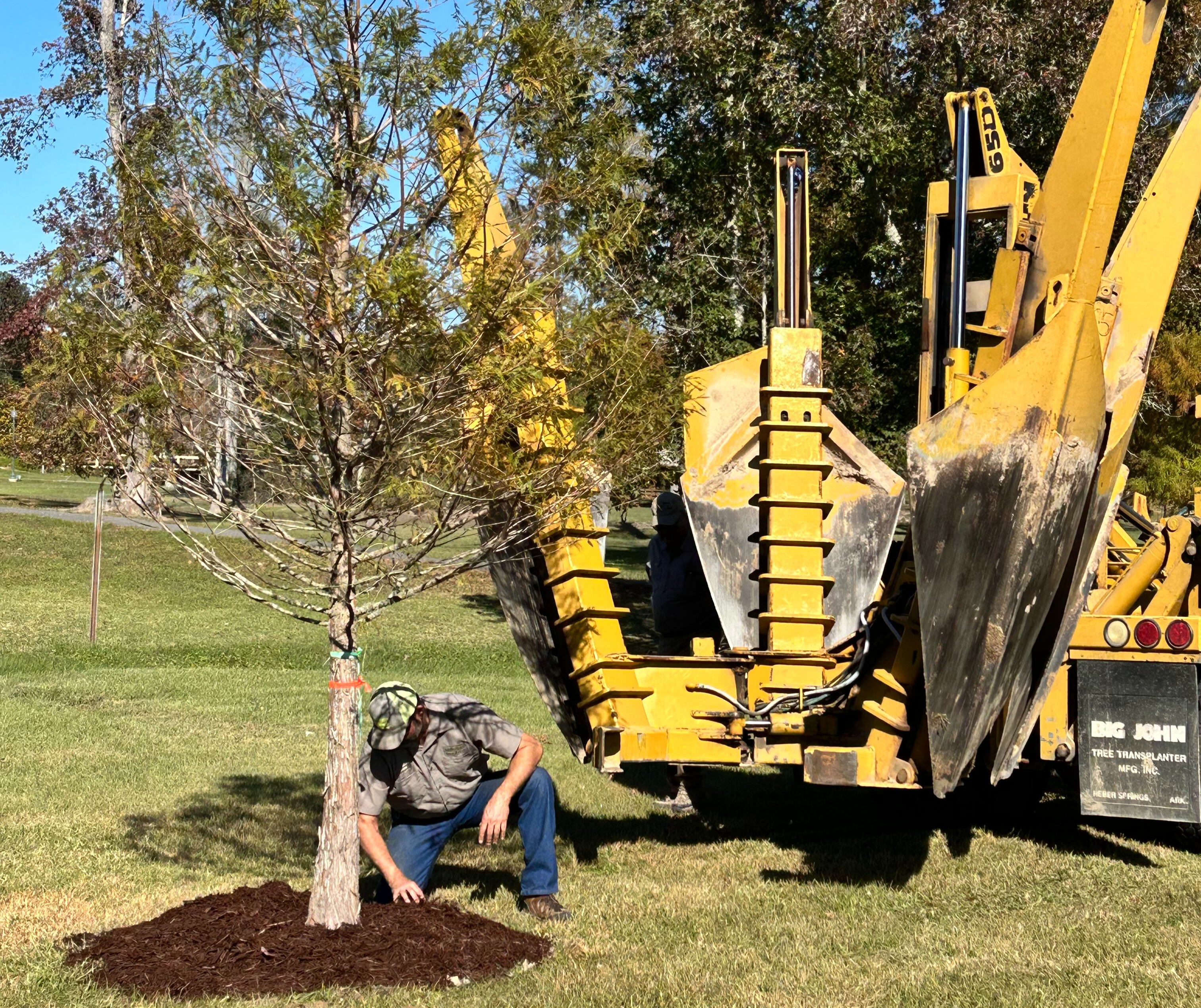 A large piece of yellow equipment sits behind a person examining soil.
