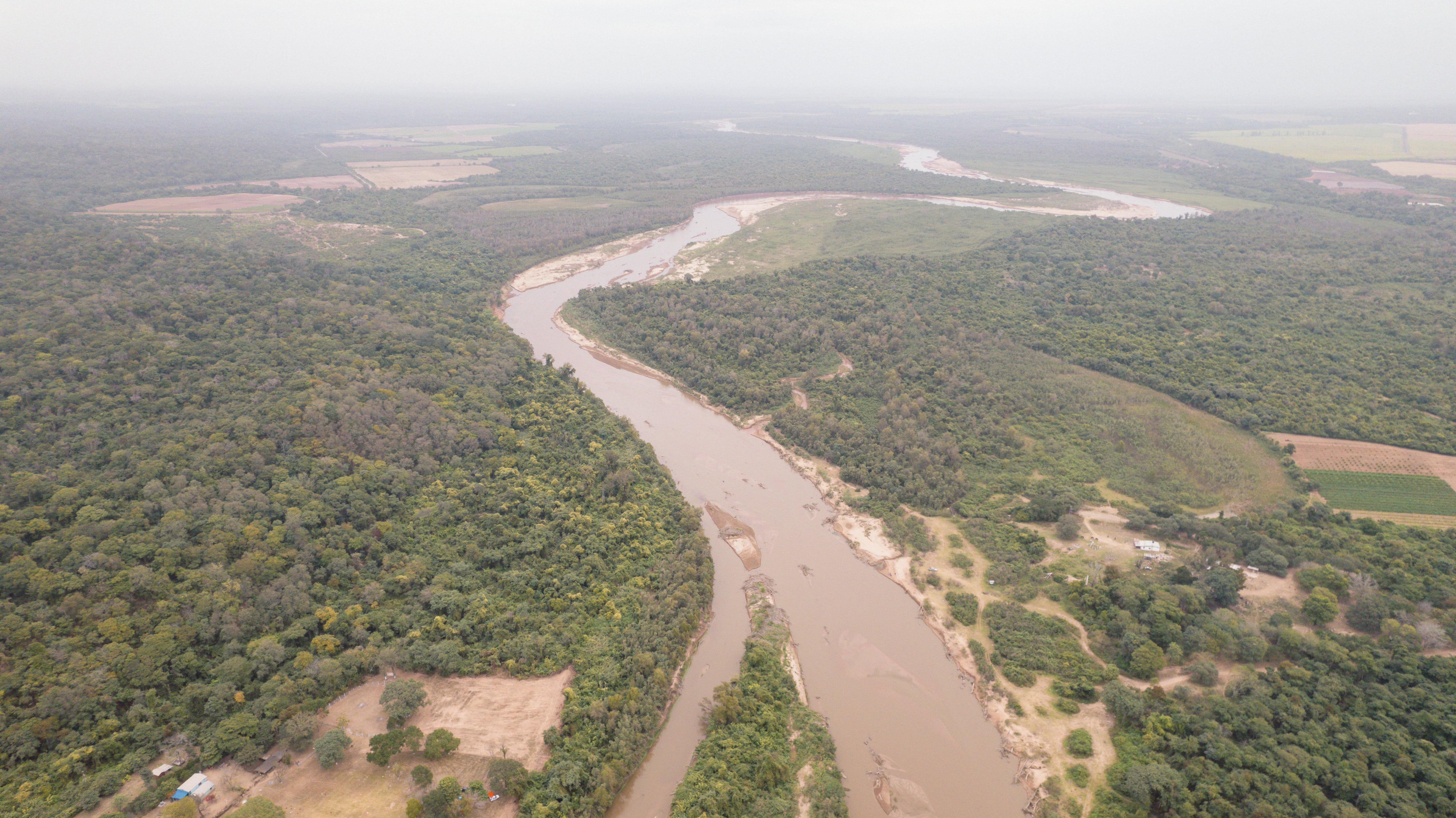 vista aerea de un rio cafe entre arbustos con neblina en el cielo. 