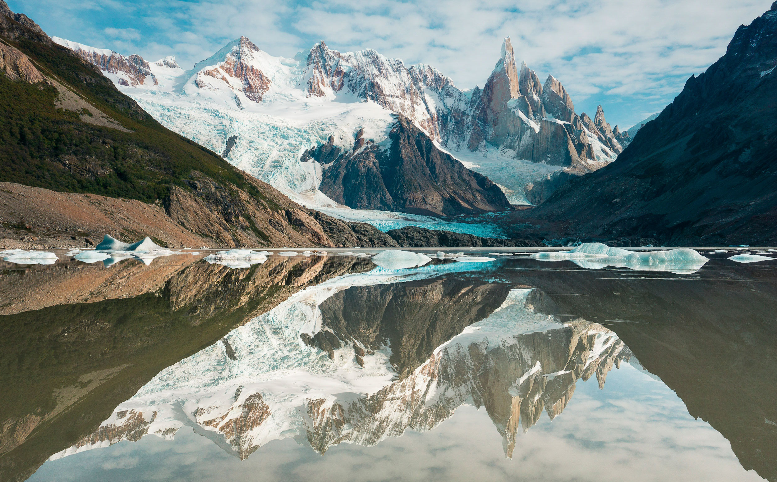 A large snow capped mountain reflects into a lake.