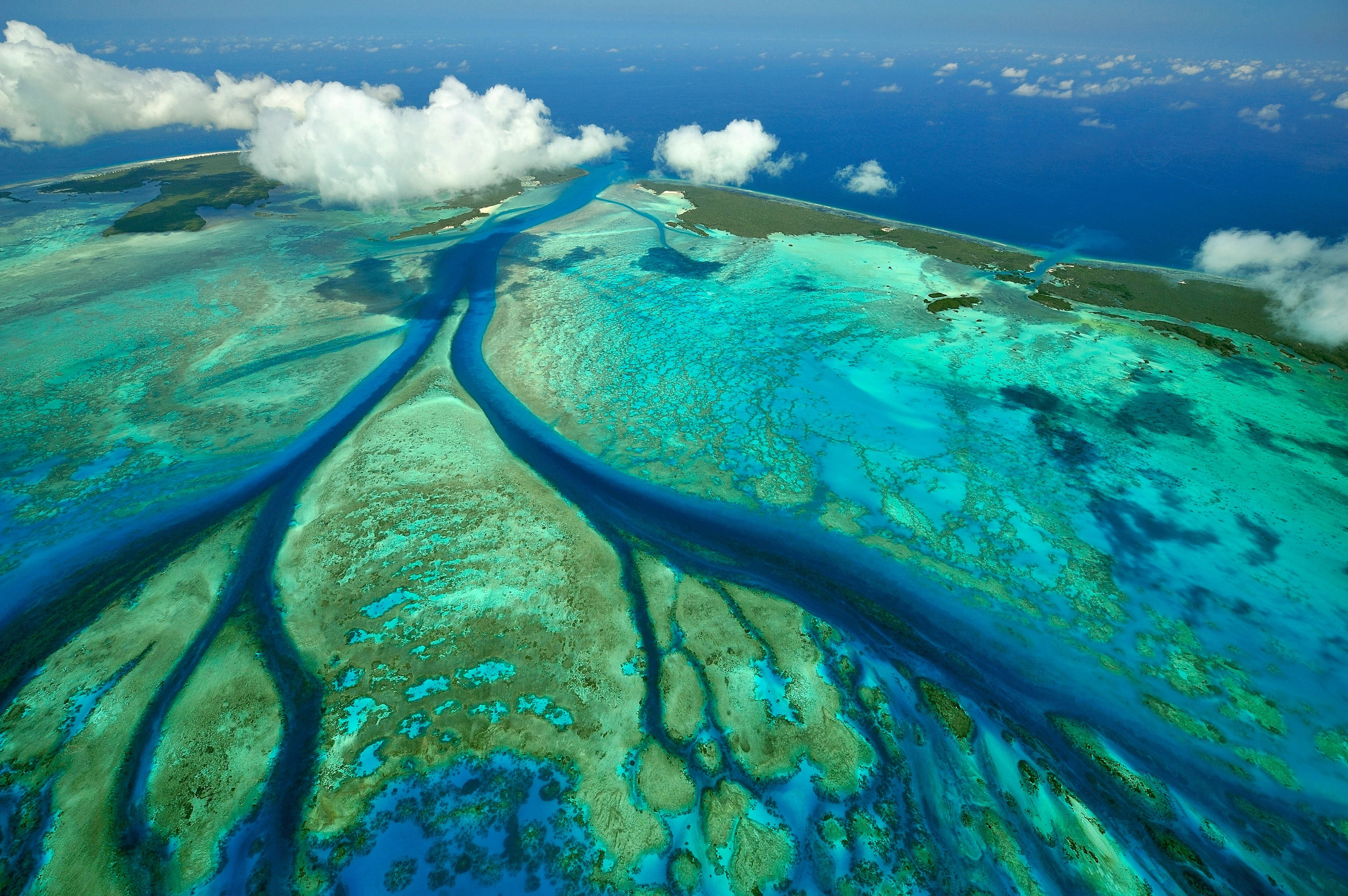 an aerial of a bright blue coastal delta dotted with clouds.