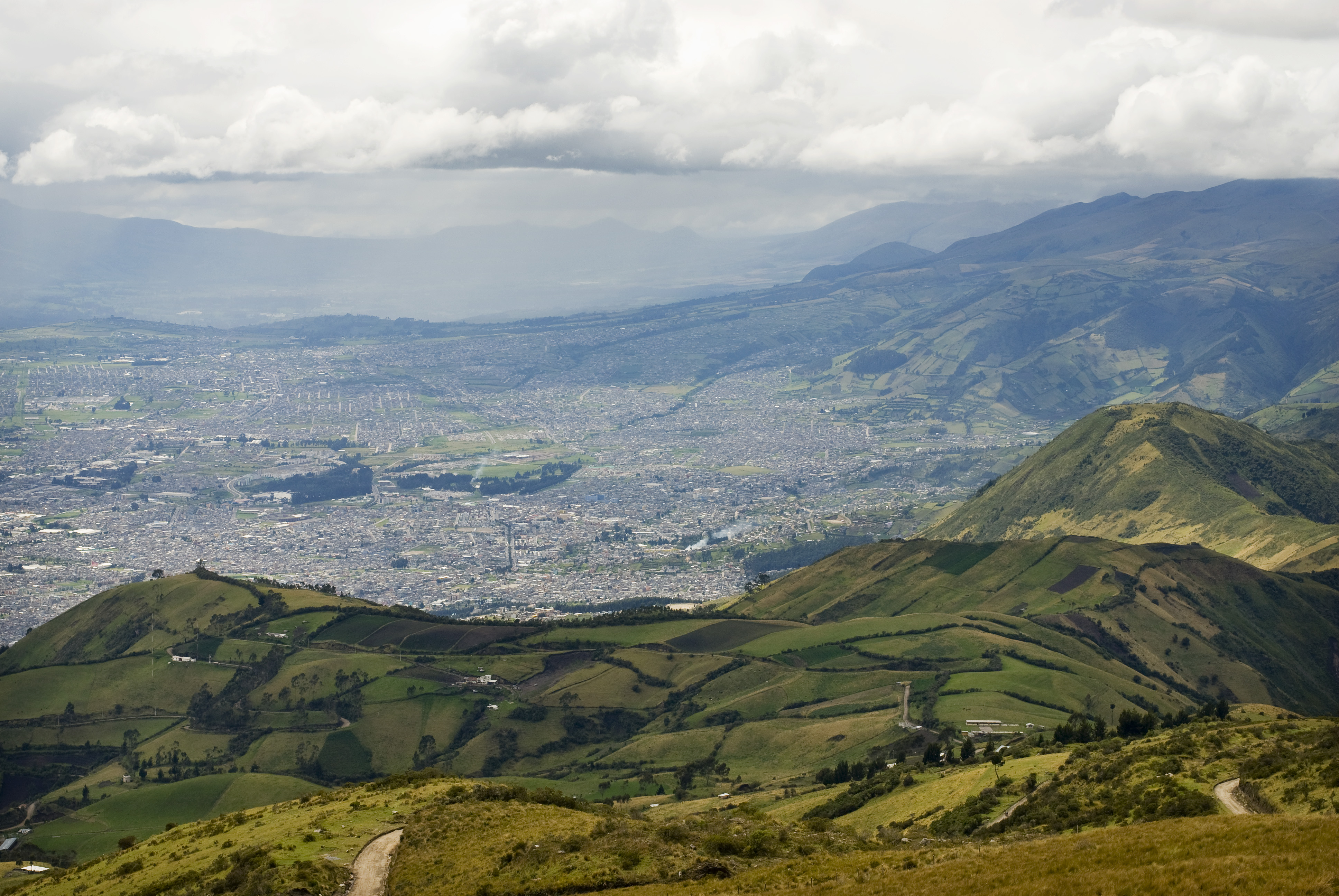 a view of the sprawling city of quito ecuador from a high point. endless city grids in the background, steep hills and rangelands in the foreground.